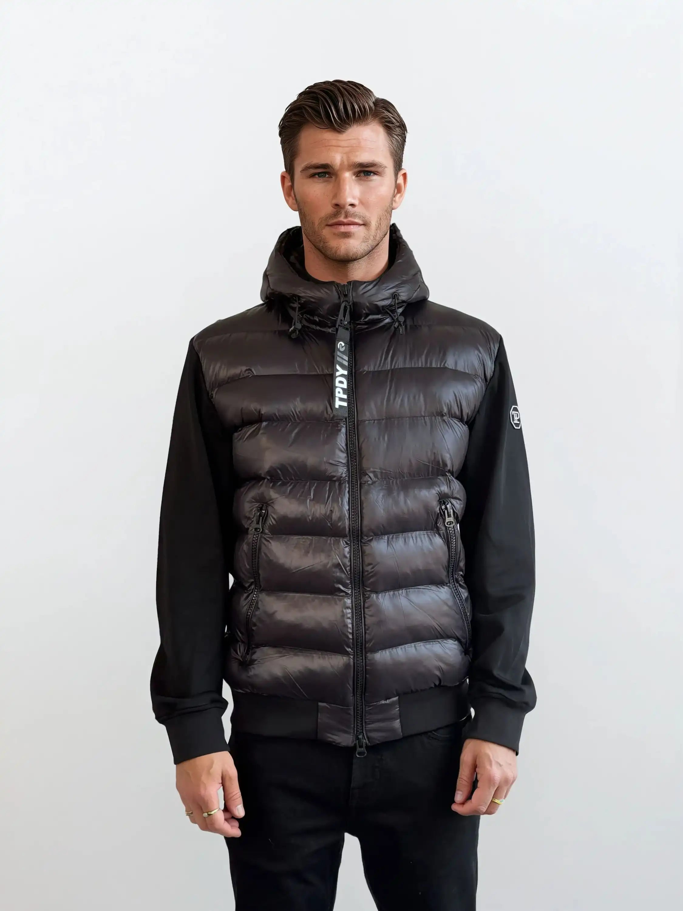 Ein Mann mit kurzen braunen Haaren trägt die trueprodigy Gesteppte Herren Übergangsjacke für urbanen City-Style, mit einem Frontreißverschluss und langen Ärmeln. Er steht mit neutralem Gesichtsausdruck vor einem schlichten hellgrauen Hintergrund.