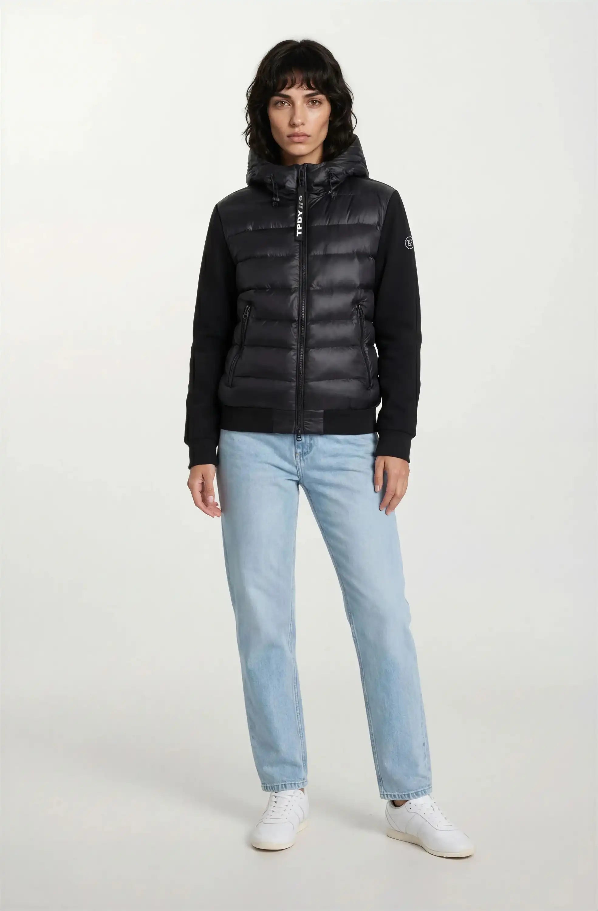 Eine Person, die eine trueprodigy Oversized Damen Bomberjacke im urbanen Materialmix-Design, hellblaue Jeans und weiße Turnschuhe trägt, steht mit dem Gesicht nach vorne vor einem schlichten weißen Hintergrund.