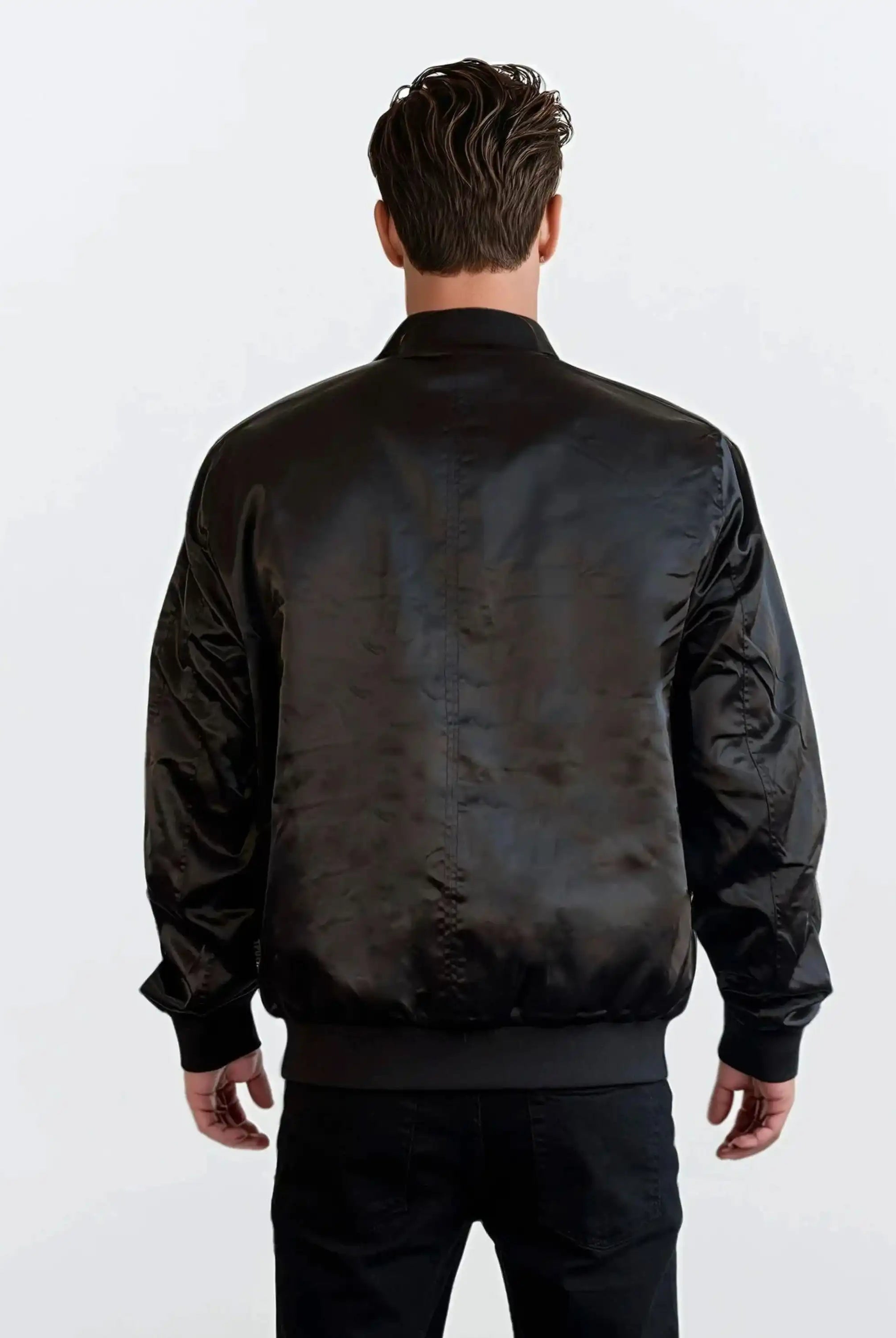 Ein Mann mit kurzen braunen Haaren steht mit dem Rücken zur Kamera und trägt eine Trueprodigy Klassische Herren Bomberjacke mit glänzender Oberfläche und eine schwarze Hose vor einem schlichten weißen Hintergrund.