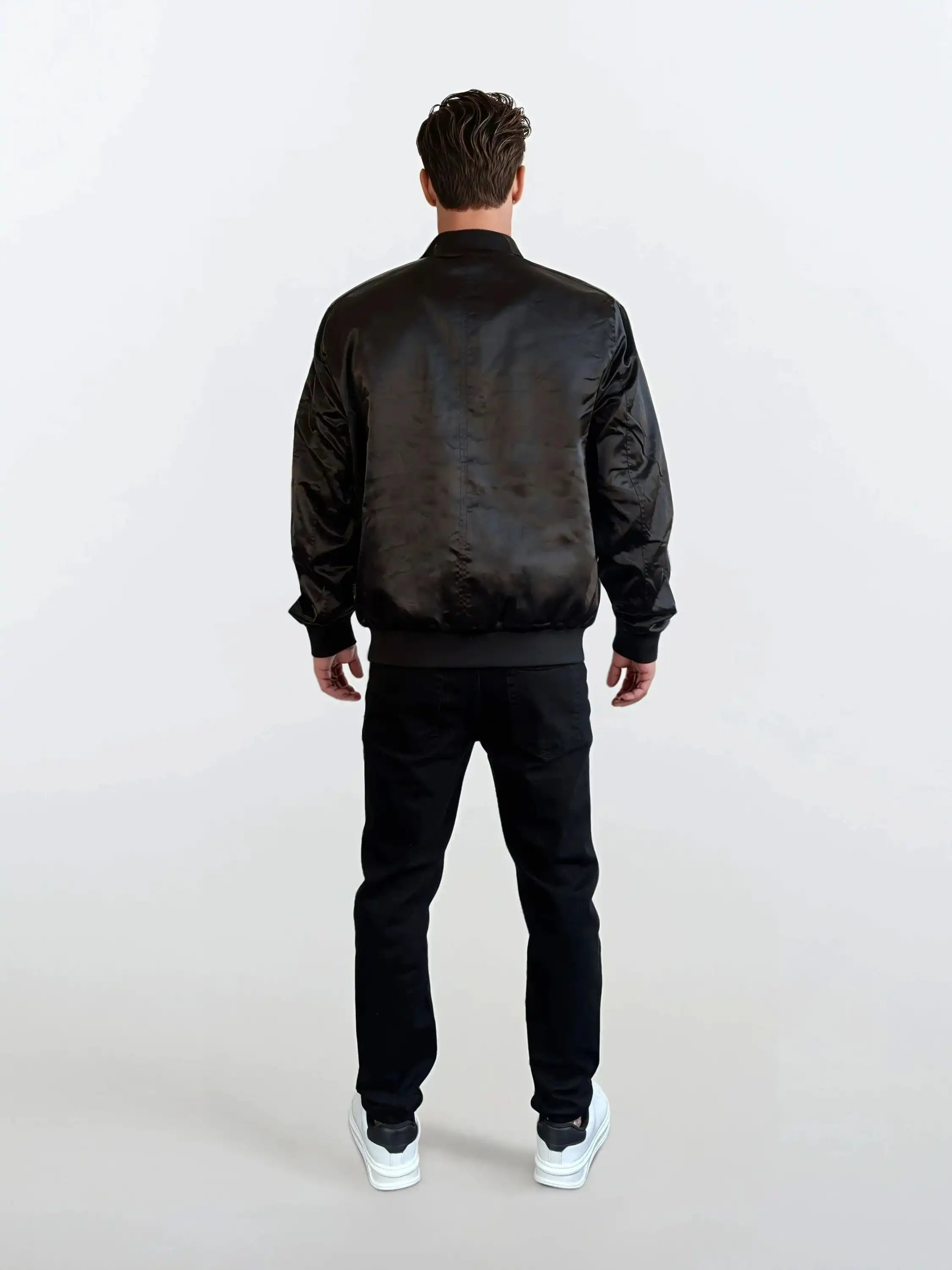 Eine Person steht mit dem Rücken zur Kamera und trägt die Klassische Herren Bomber Jacke mit glänzender Oberfläche von trueprodigy, schwarzen Hosen und weißen Sneakers - ein urbaner Look vor hellem, schlichten Hintergrund.