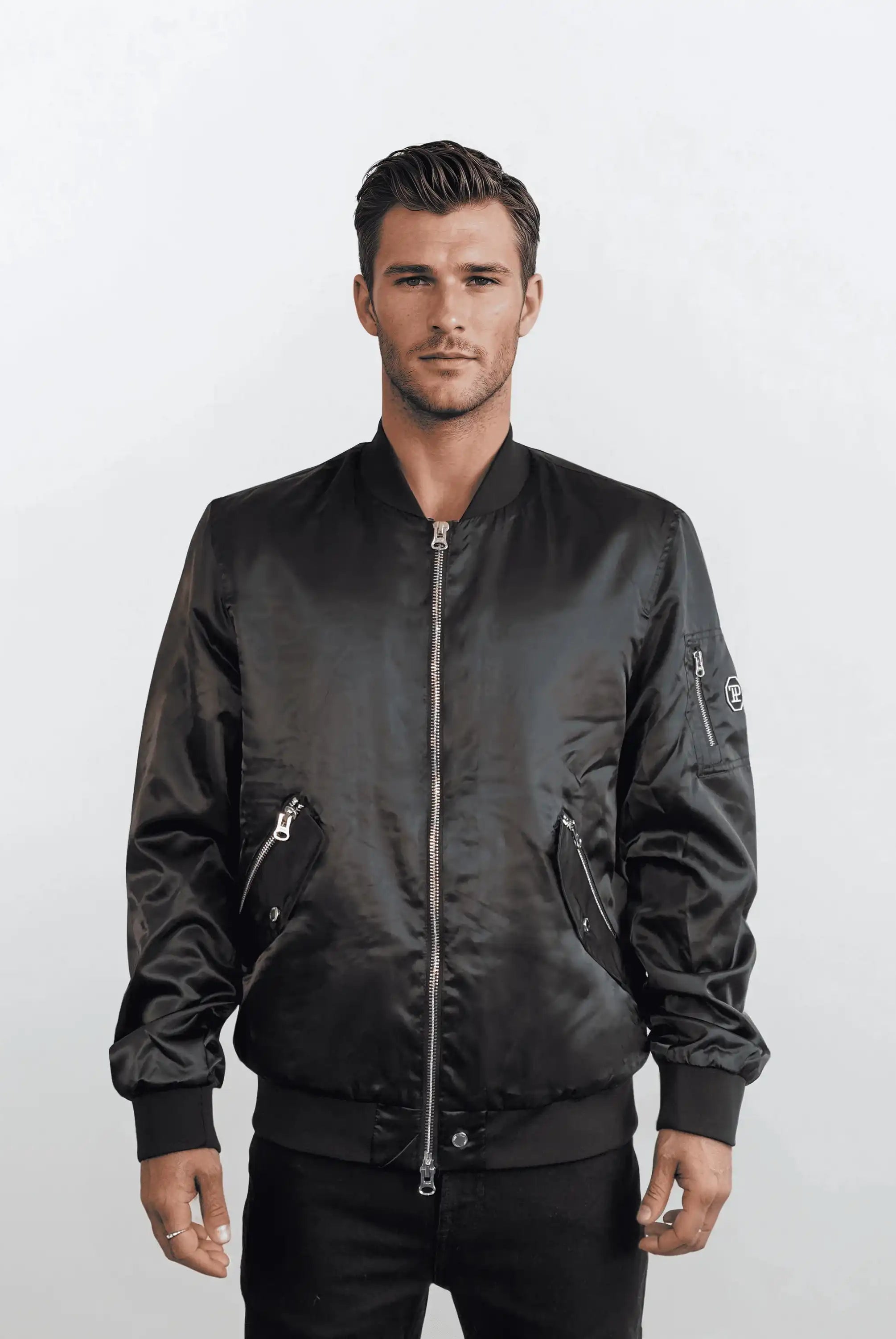 Ein Mann mit kurzen braunen Haaren modelliert die trueprodigy Klassische Herren Bomberjacke mit glänzender Oberfläche. Er steht vor einem weißen Hintergrund mit einer entspannten Pose und einem neutralen Ausdruck und verkörpert den urbanen Stil.