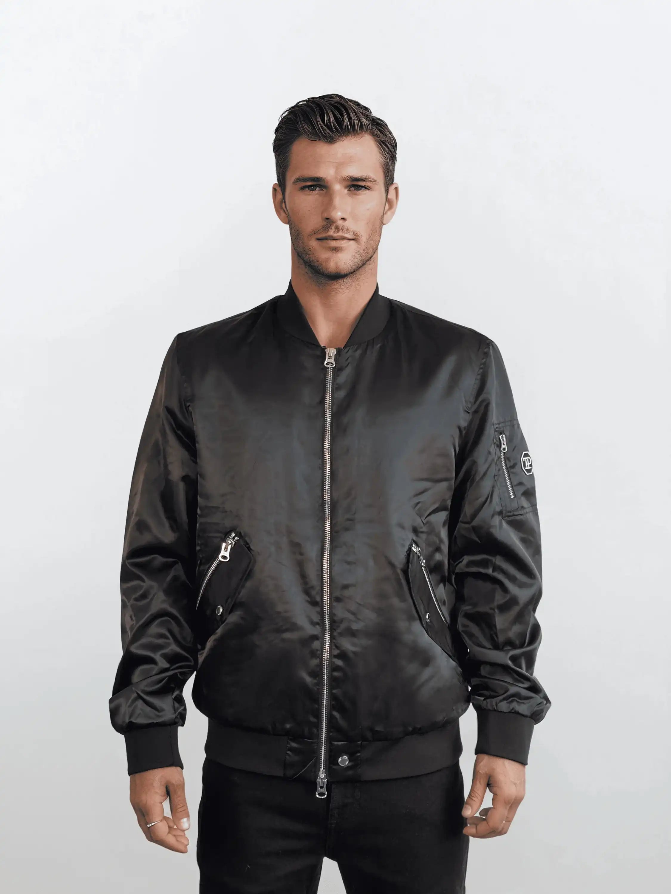 Ein Mann mit kurzen braunen Haaren modelliert die trueprodigy Klassische Herren Bomberjacke mit glänzender Oberfläche. Er steht vor einem weißen Hintergrund mit einer entspannten Pose und einem neutralen Ausdruck und verkörpert den urbanen Stil.