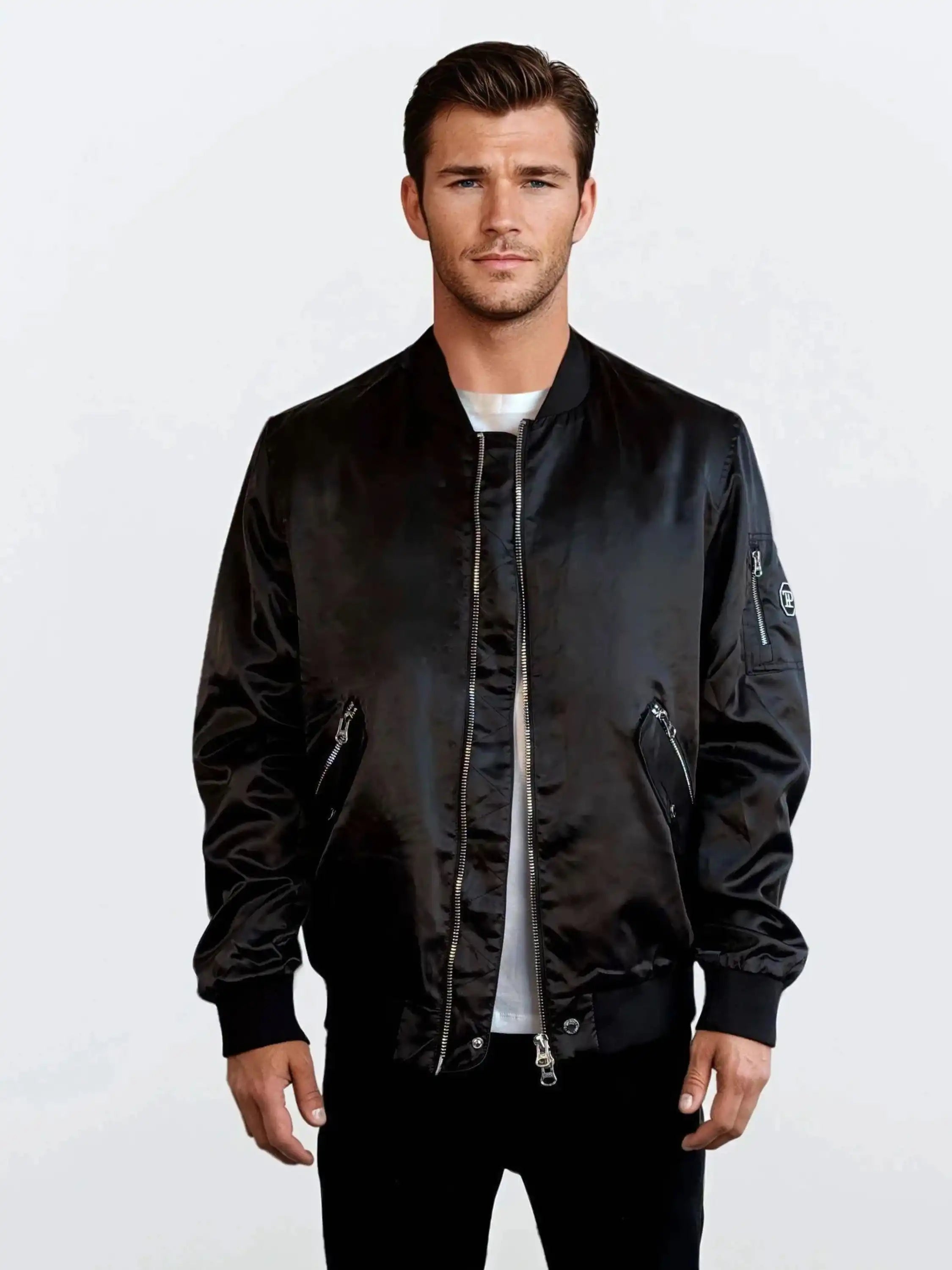 Ein Mann steht vor einem schlichten weißen Hintergrund und trägt eine trueprodigy Klassische Herren Bomberjacke mit glänzender Oberfläche über einem weißen T-Shirt. Die Jacke hat Reißverschlusstaschen, gerippte Bündchen und einen gerippten Saum, was ihr einen urbanen Stil verleiht.