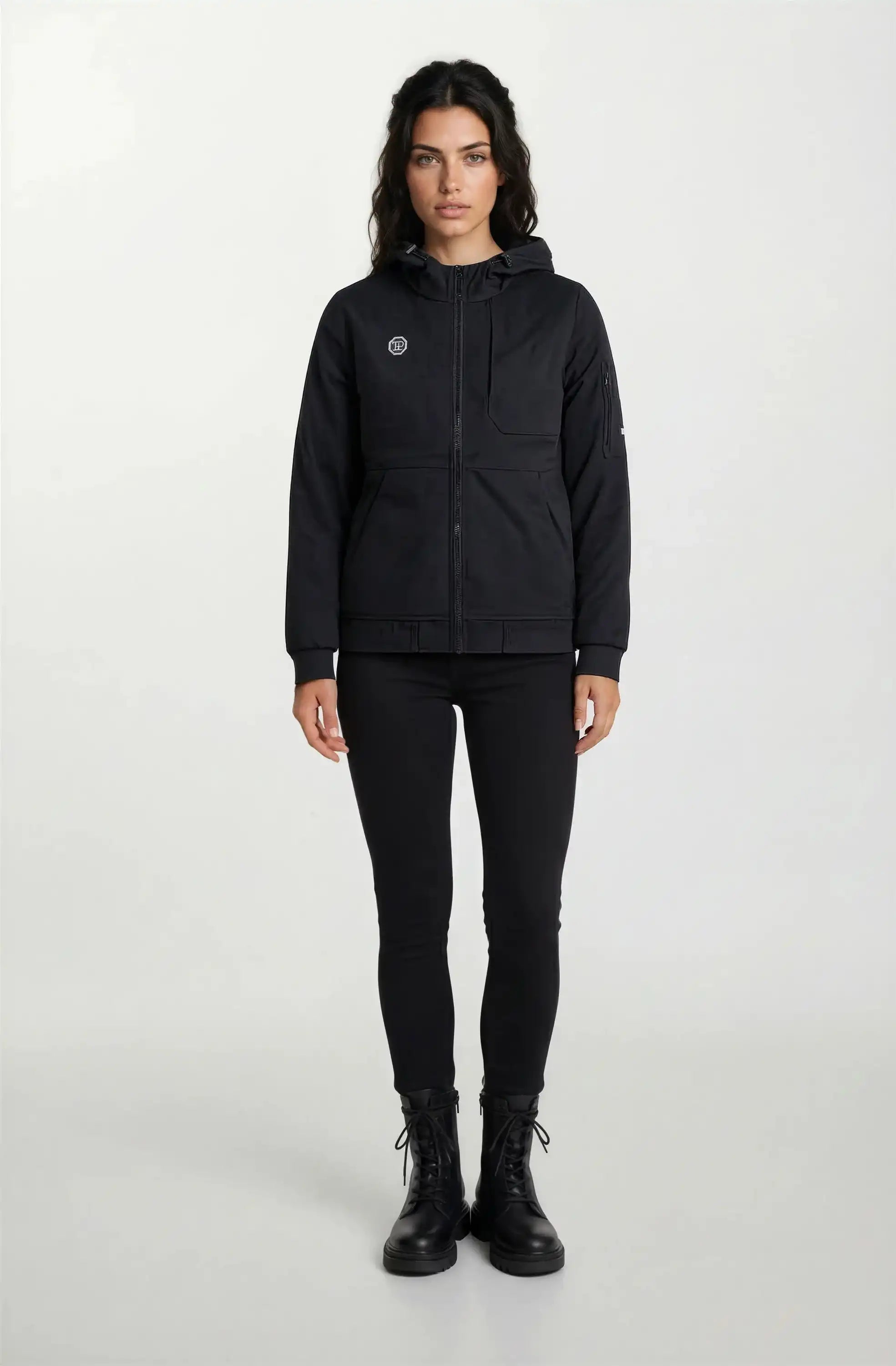 Eine Person steht mit dem Gesicht nach vorne vor einem schlichten Hintergrund. Sie trägt die Trueprodigy Leichte Herrenjacke mit Brust- und Ärmelbadge, passende schwarze Hosen und Schnürstiefel. Die Hände liegen entspannt an der Seite.