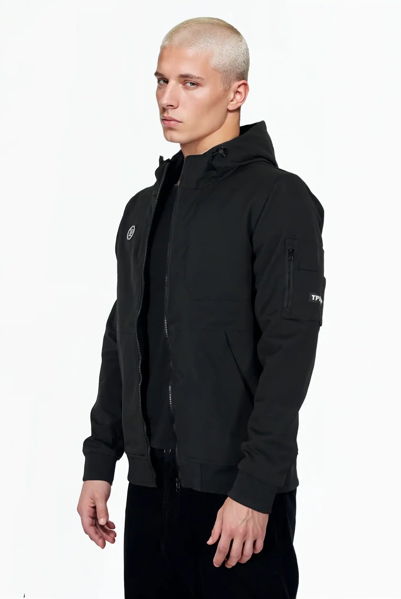 Eine Person mit kurzen, gebleichten blonden Haaren trägt das Lucas Leichte Herrenjacke mit Brust- und Ärmelbadge von trueprodigy mit einem Reißverschluss, zwei Brusttaschen und einem Ärmelaufnäher vor einem schlichten weißen Hintergrund.