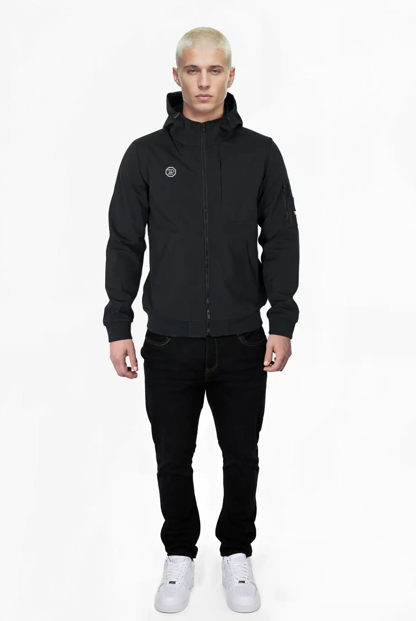 Eine Person mit kurzen blonden Haaren blickt nach vorne und trägt die Trueprodigy Lucas Leichte Herrenjacke mit Brust- und Ärmelbadge, schwarze Jeans und weiße Turnschuhe vor einem schlichten weißen Hintergrund.