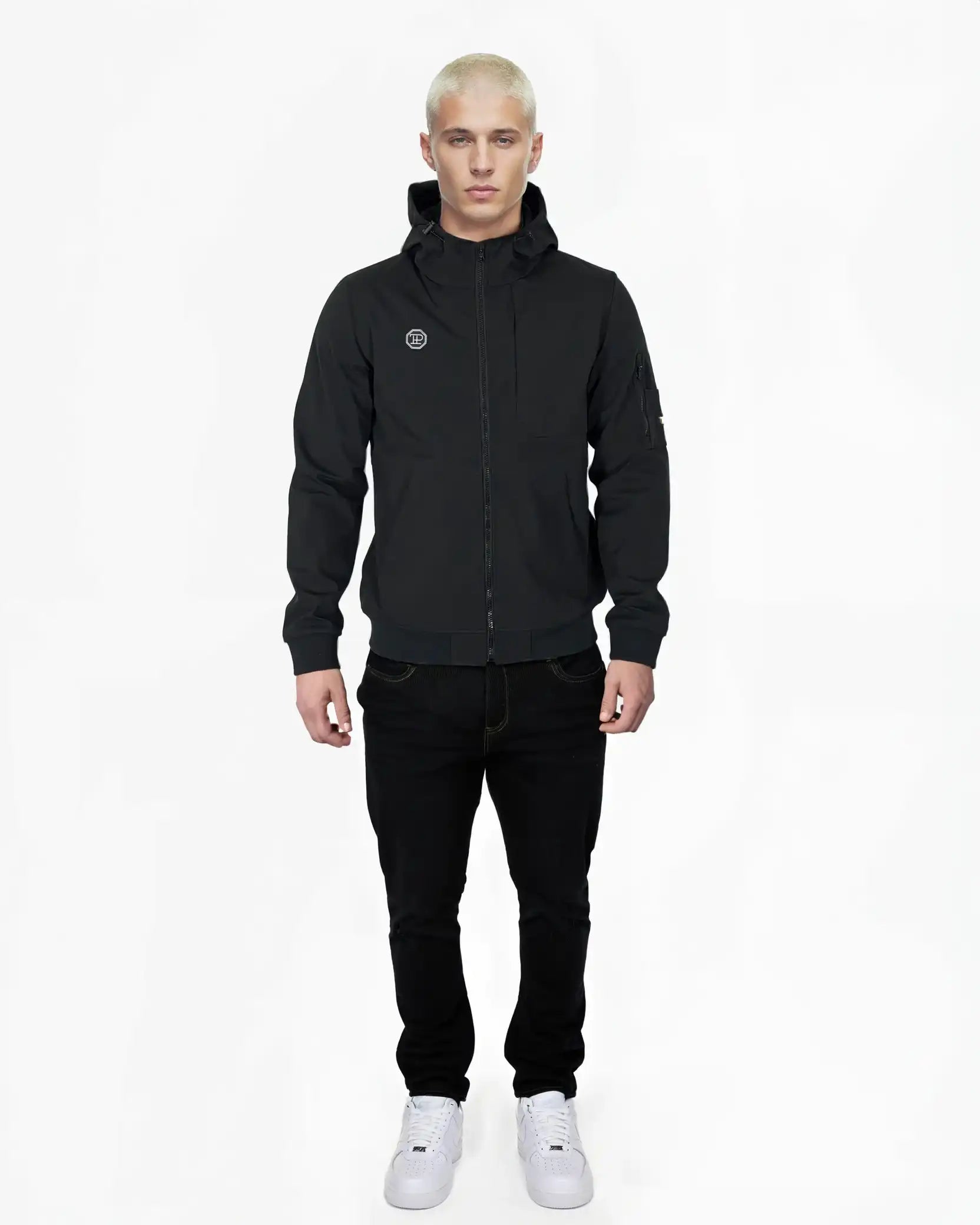 Eine Person mit kurzen blonden Haaren blickt nach vorne und trägt die Trueprodigy Lucas Leichte Herrenjacke mit Brust- und Ärmelbadge, schwarze Jeans und weiße Turnschuhe vor einem schlichten weißen Hintergrund.