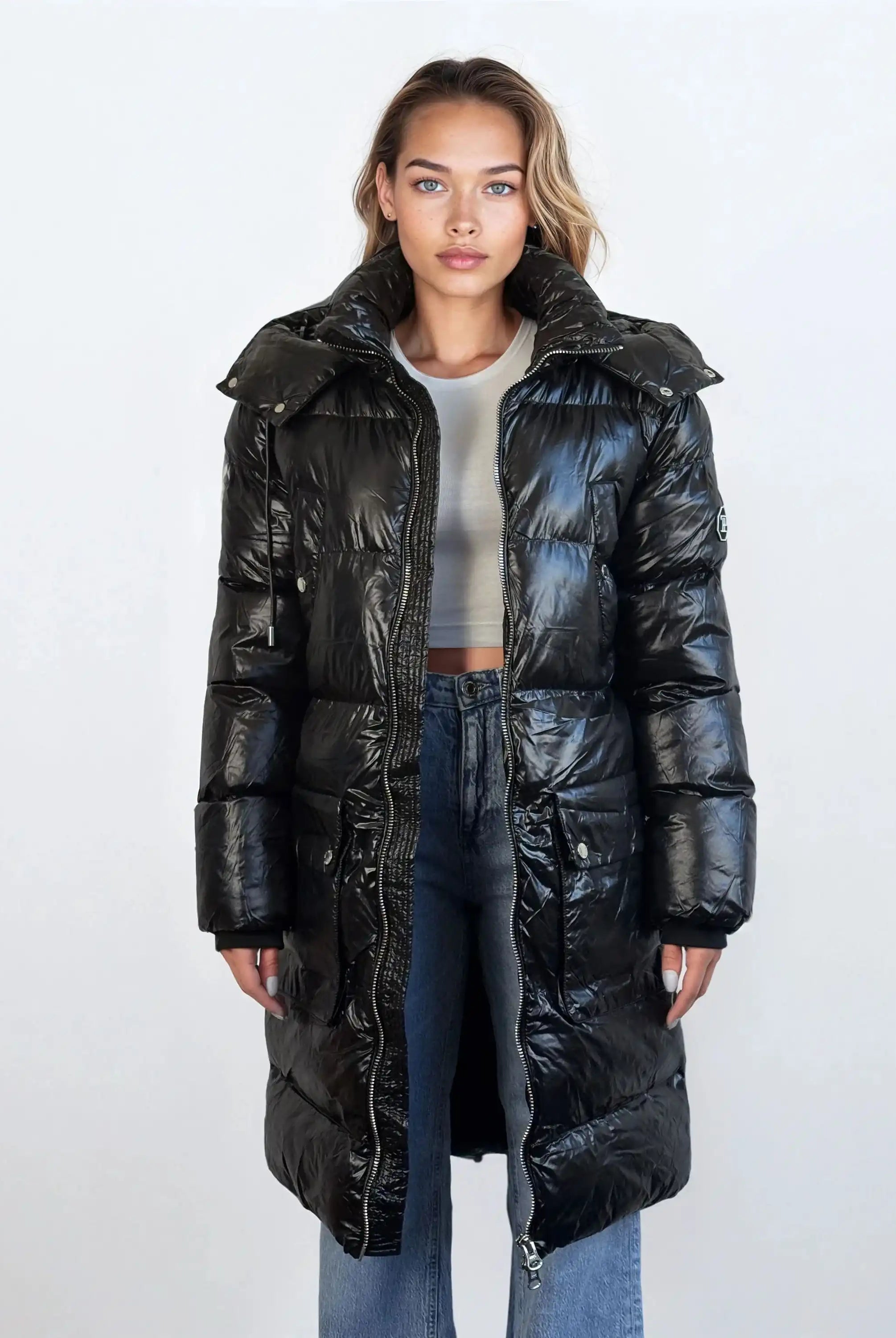Eine nach vorne blickende Person trägt die trueprodigy Damen Winterjacke mit abnehmbarer Kapuze im Regular Fit über einem hellgrauen Crop Top und blauen Jeans vor einem schlichten hellen Hintergrund.