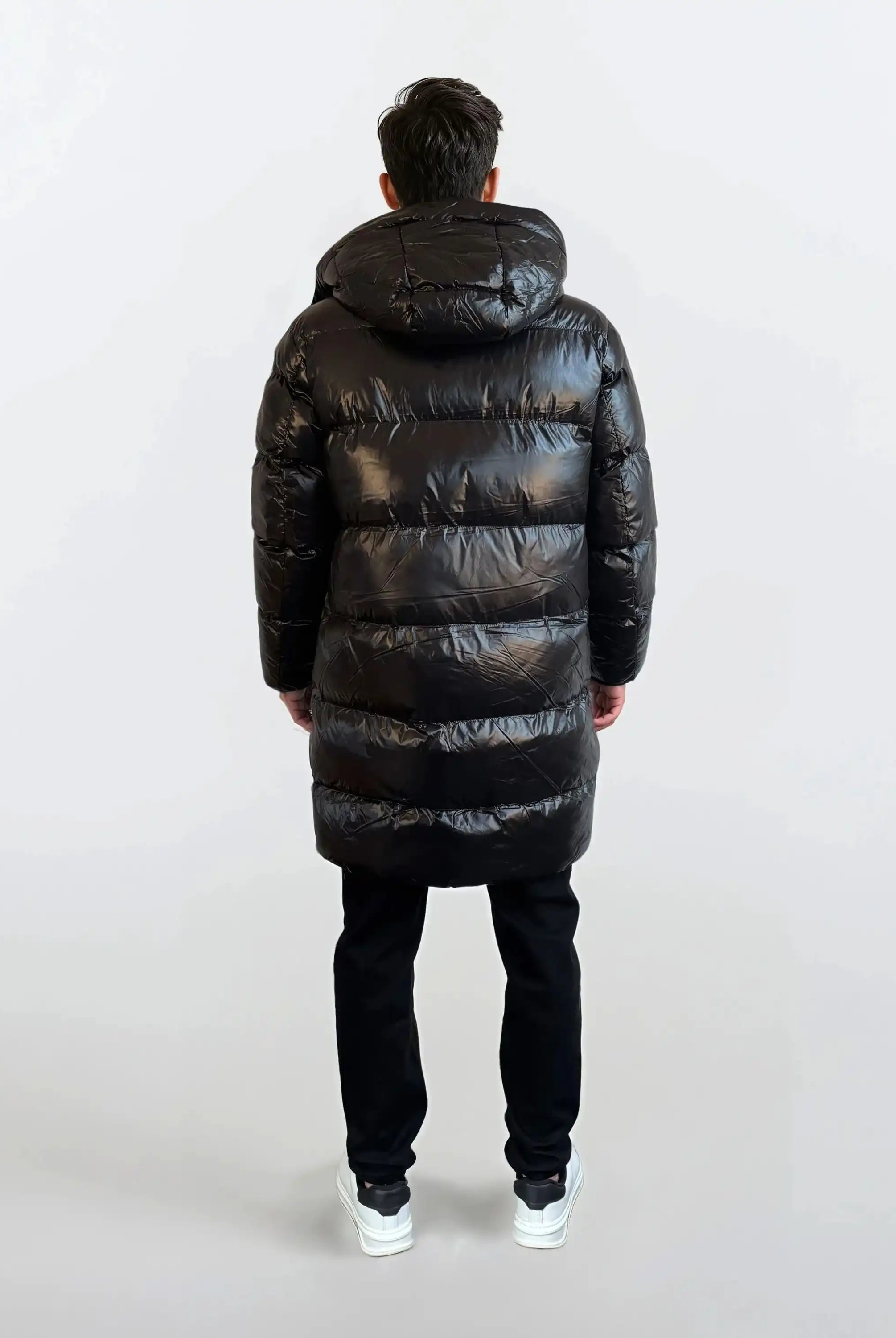 Eine Person mit kurzen dunklen Haaren schaut von der Kamera weg und trägt eine glänzende trueprodigy Herren Winterjacke mit abnehmbarer Kapuze im Regular Fit, eine schwarze Hose und weiße Turnschuhe vor einem schlichten hellen Hintergrund.