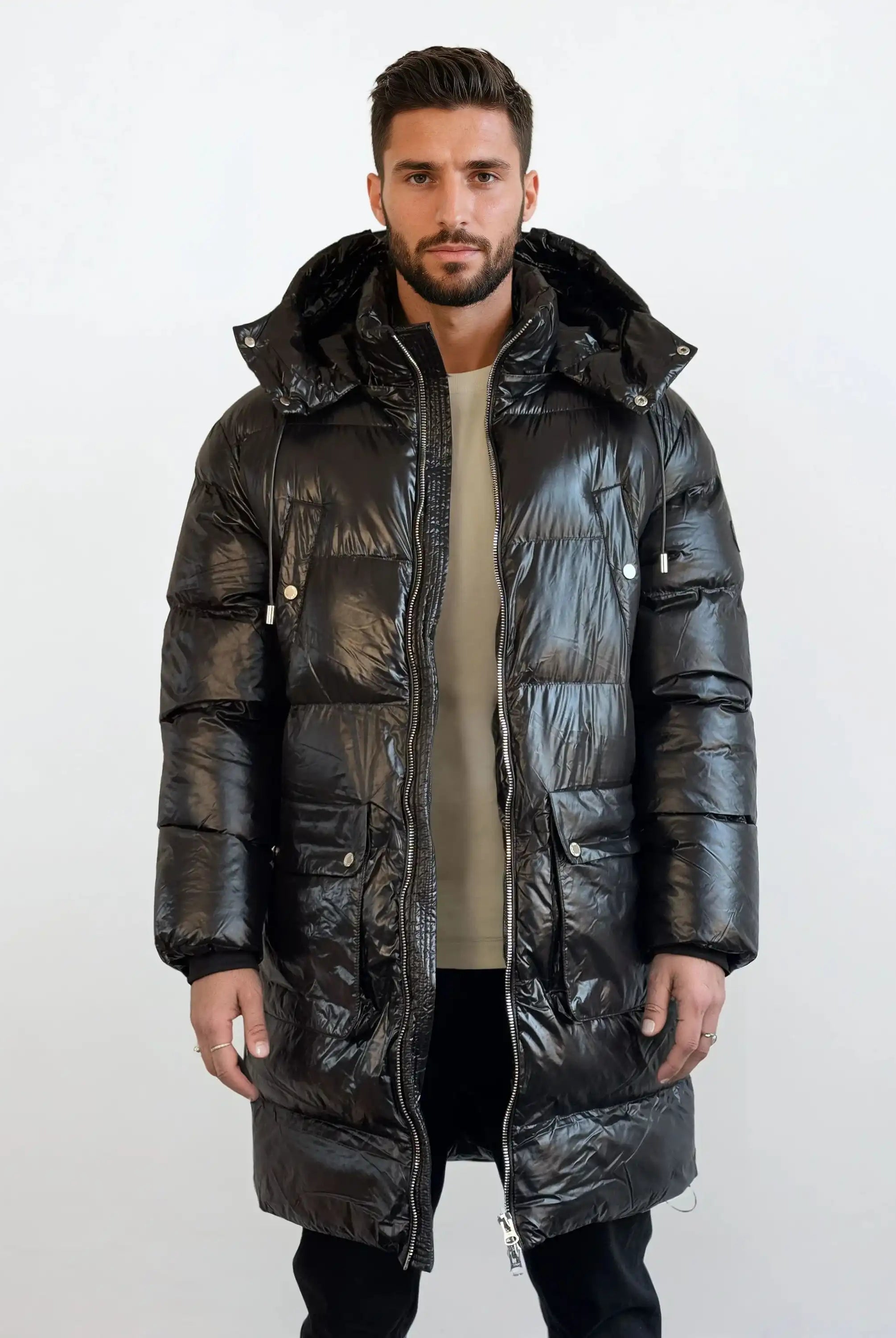 Ein Mann steht mit dem Gesicht nach vorne und trägt eine glänzende trueprodigy Herren Winterjacke mit abnehmbarer Kapuze im Regular Fit über einem beigen Hemd und einer schwarzen Hose vor einem schlichten weißen Hintergrund.