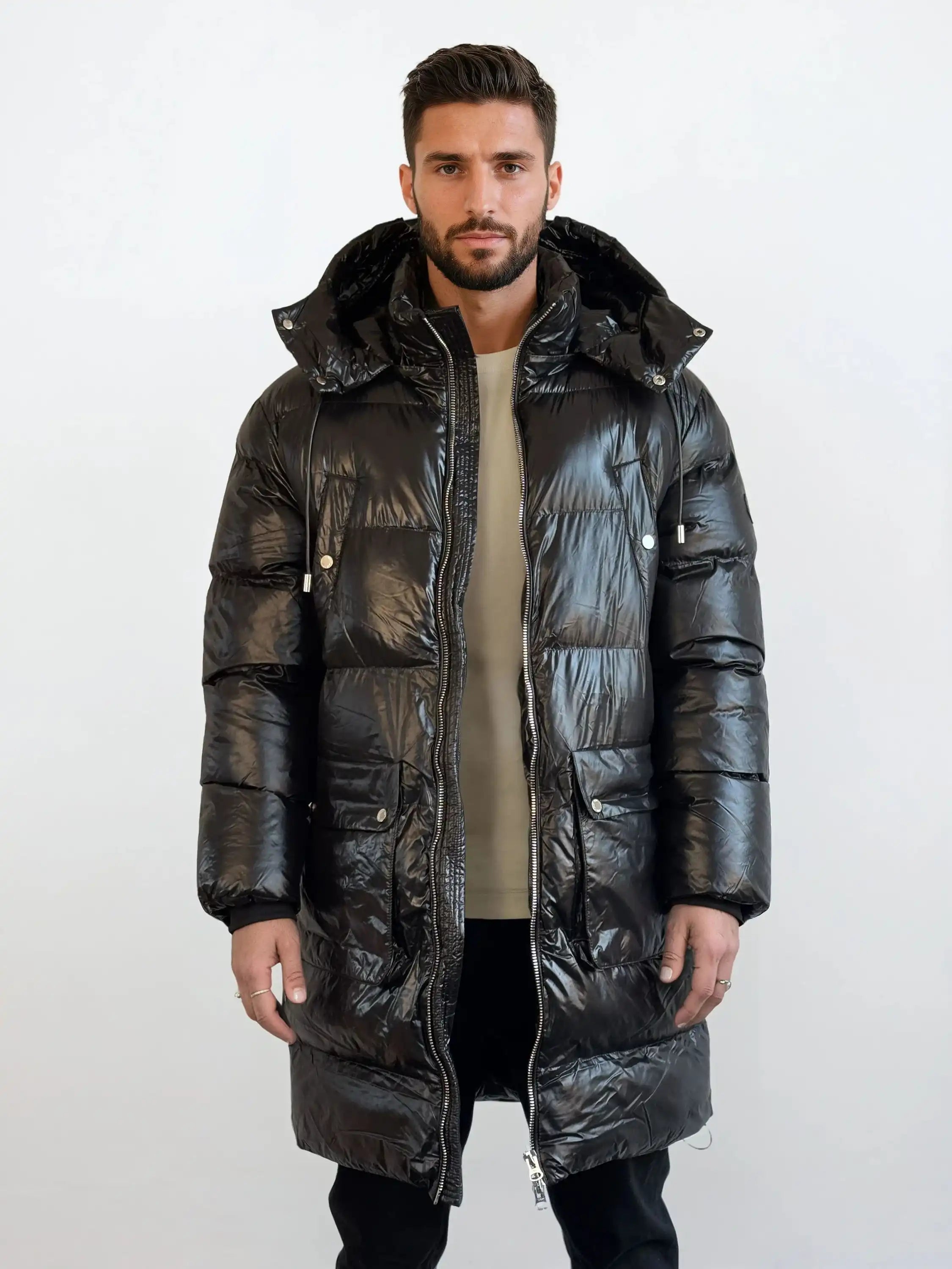 Ein Mann steht mit dem Gesicht nach vorne und trägt eine glänzende trueprodigy Herren Winterjacke mit abnehmbarer Kapuze im Regular Fit über einem beigen Hemd und einer schwarzen Hose vor einem schlichten weißen Hintergrund.