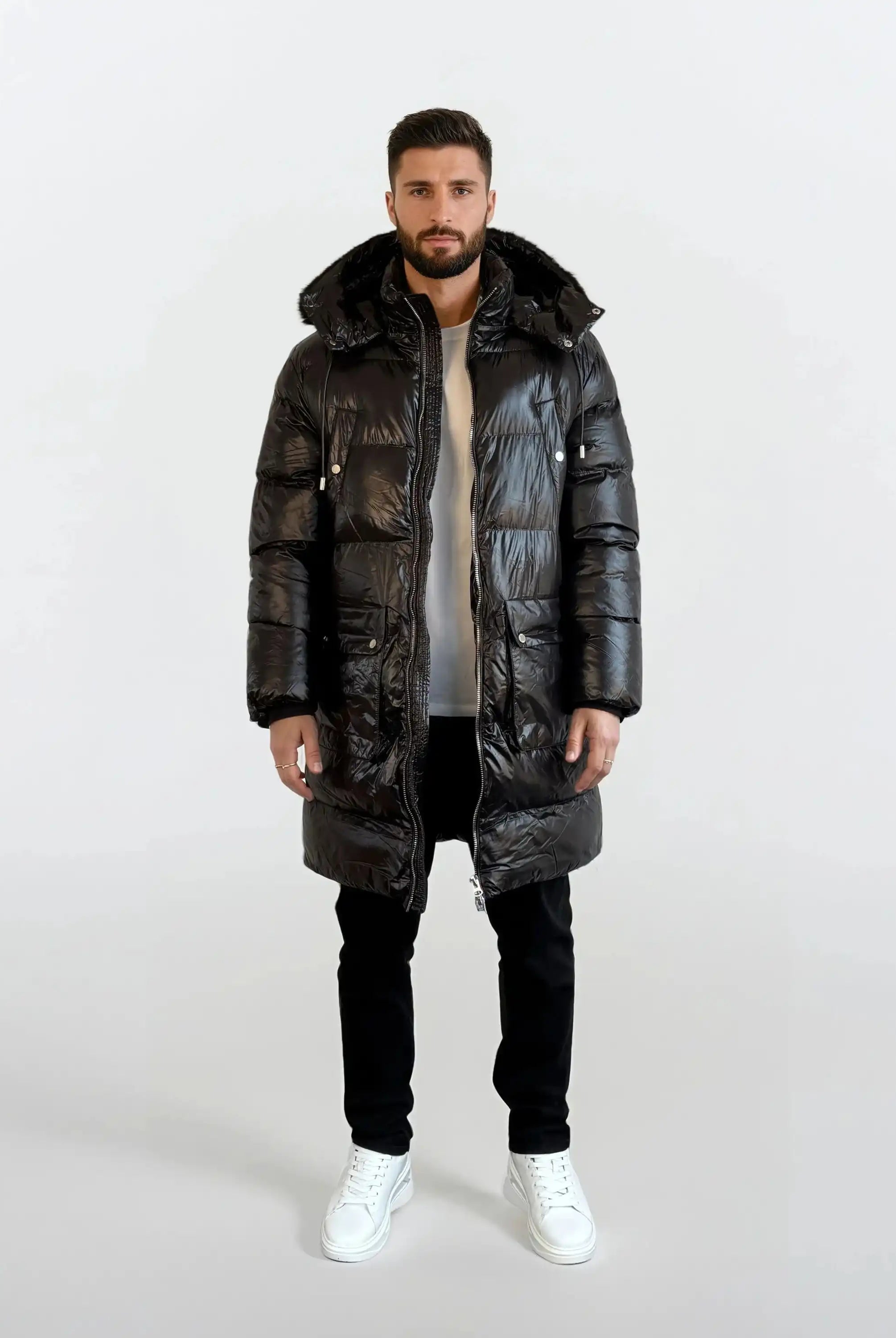 Ein Mann steht mit dem Gesicht nach vorne und trägt eine glänzende trueprodigy Herren Winterjacke mit abnehmbarer Kapuze im Regular Fit über einem weißen Hemd, einer schwarzen Hose und weißen Turnschuhen vor einem schlichten weißen Hintergrund.