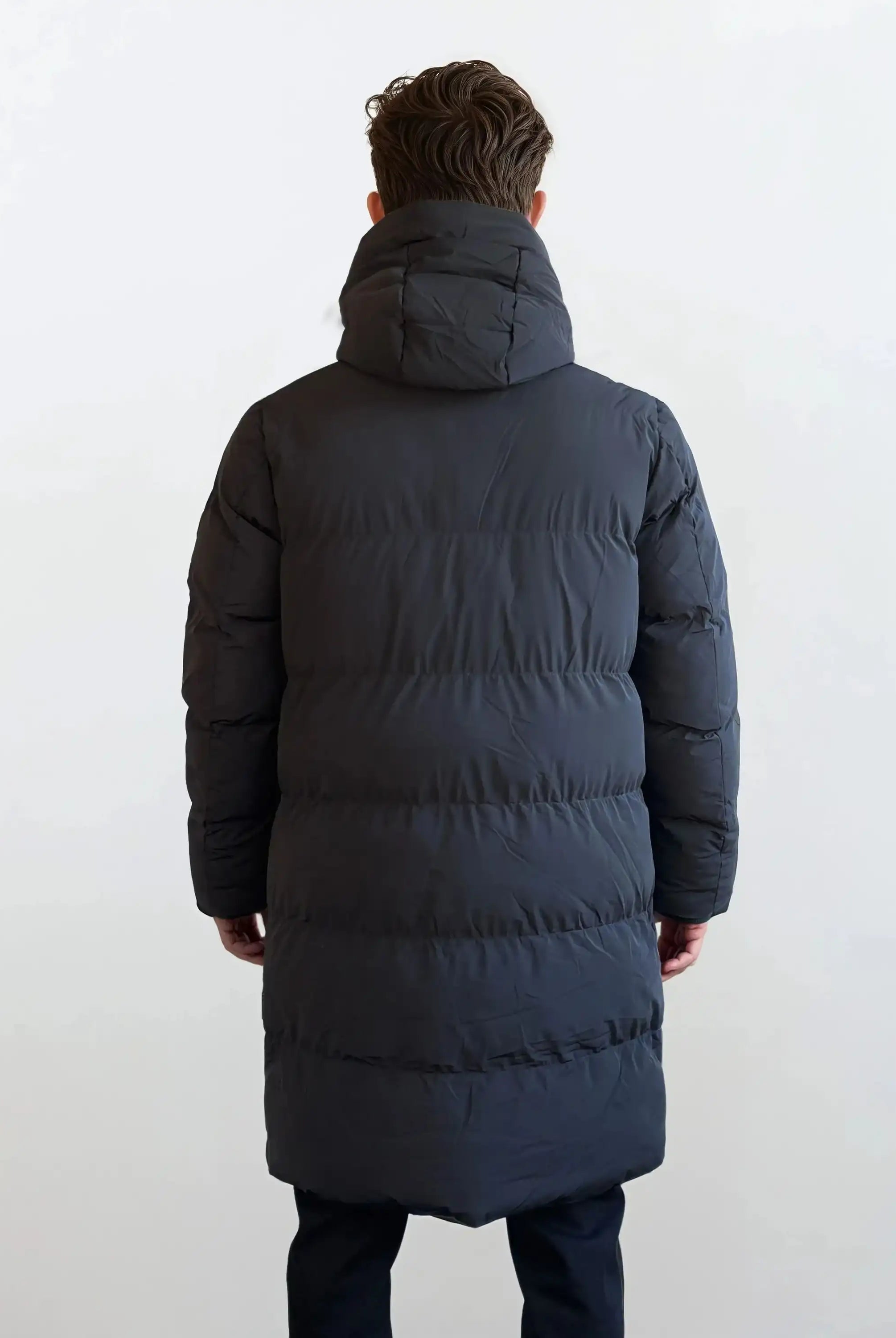 Eine Person steht mit dem Rücken zur Kamera und trägt den Herren Parka mit fester Kapuze im Regular Fit von trueprodigy; der wasserabweisende Mantel hebt sich vor einem schlichten, hellen Hintergrund ab.