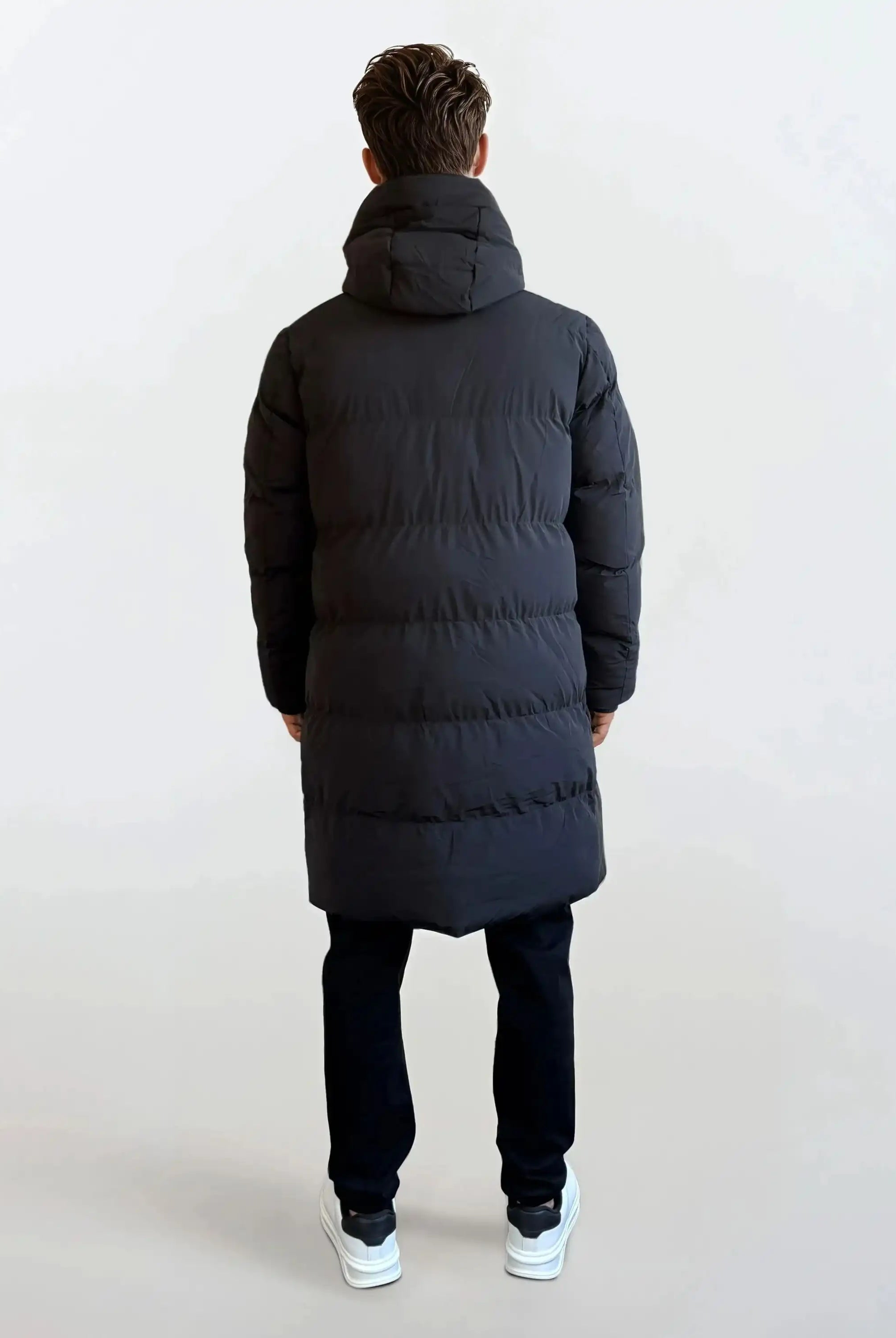 Eine Person steht von der Kamera abgewandt und trägt den trueprodigy Herren Parka mit fester Kapuze im Regular Fit, schwarze Hose und weiße Sneaker vor einem schlichten hellen Hintergrund.