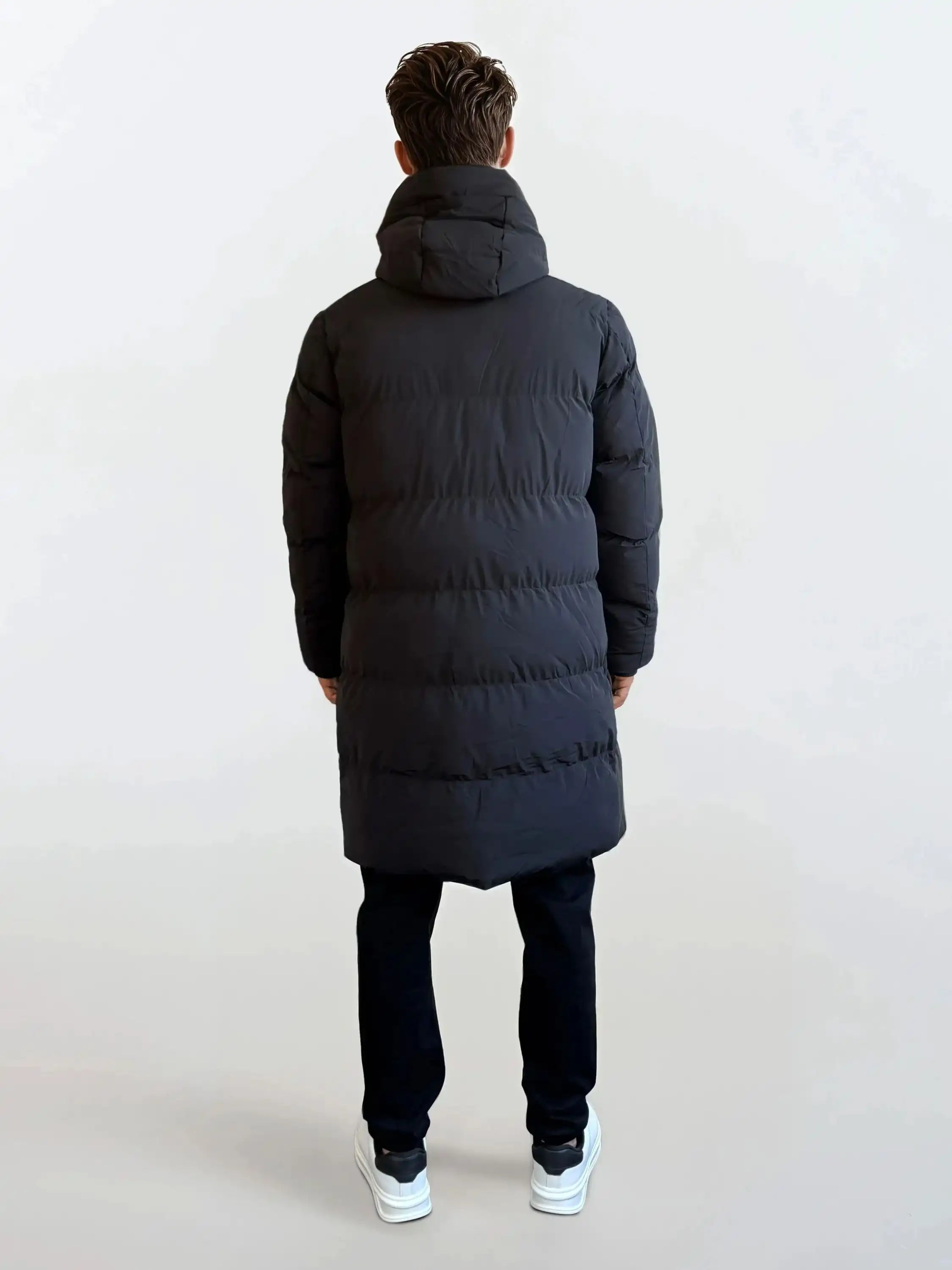 Eine Person steht von der Kamera abgewandt und trägt den trueprodigy Herren Parka mit fester Kapuze im Regular Fit, schwarze Hose und weiße Sneaker vor einem schlichten hellen Hintergrund.