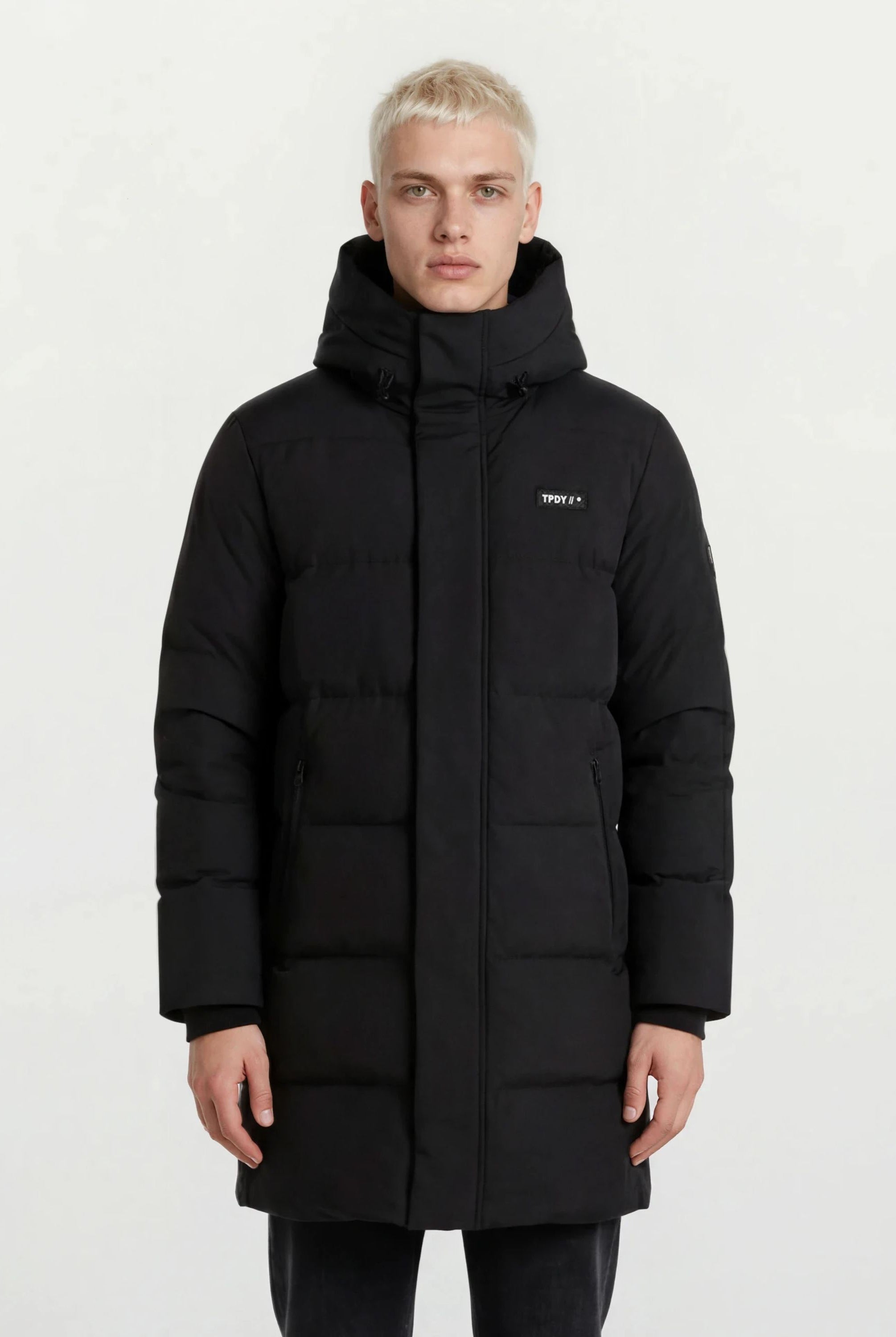 Ein Mann trägt den trueprodigy Herren Parka mit fester Kapuze im Regular Fit in Schwarz, mit kleinem Logo auf der linken Brust und seitlichen Reißverschlusstaschen, vor einem schlichten weißen Hintergrund. Der Mantel ist wasserabweisend.