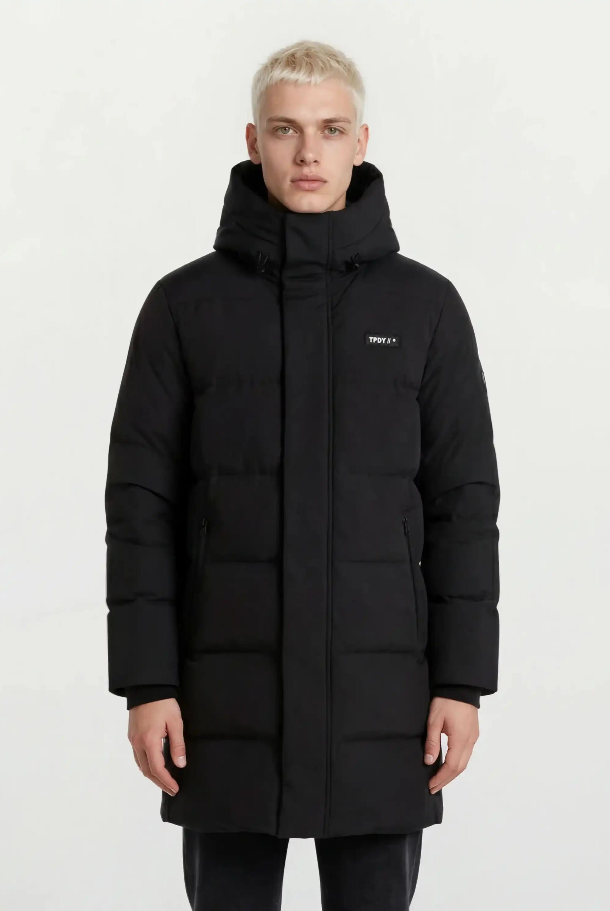 Ein Mann trägt den trueprodigy Herren Parka mit fester Kapuze im Regular Fit in Schwarz, mit kleinem Logo auf der linken Brust und seitlichen Reißverschlusstaschen, vor einem schlichten weißen Hintergrund. Der Mantel ist wasserabweisend.