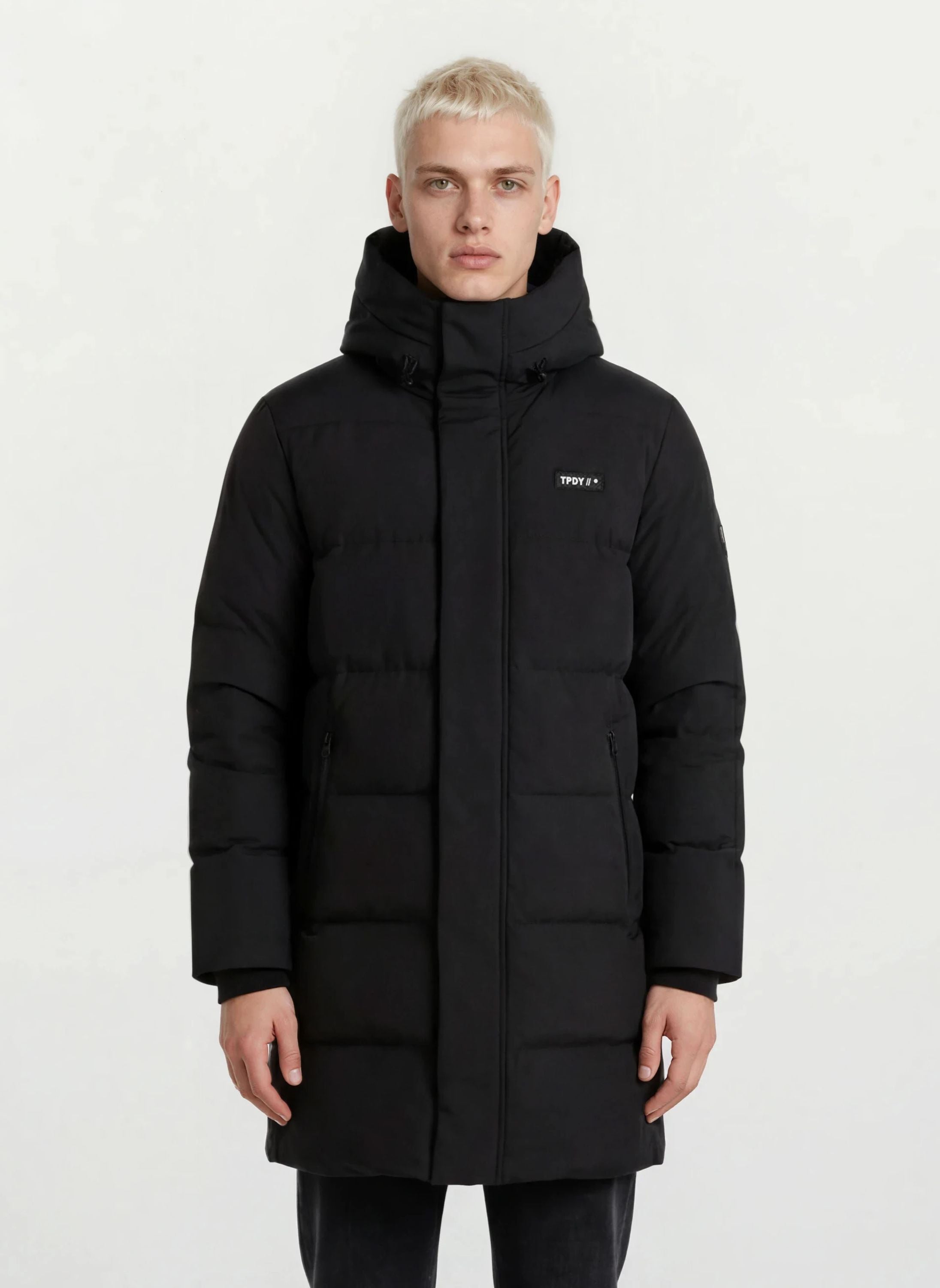 Ein Mann trägt den trueprodigy Herren Parka mit fester Kapuze im Regular Fit in Schwarz, mit kleinem Logo auf der linken Brust und seitlichen Reißverschlusstaschen, vor einem schlichten weißen Hintergrund. Der Mantel ist wasserabweisend.