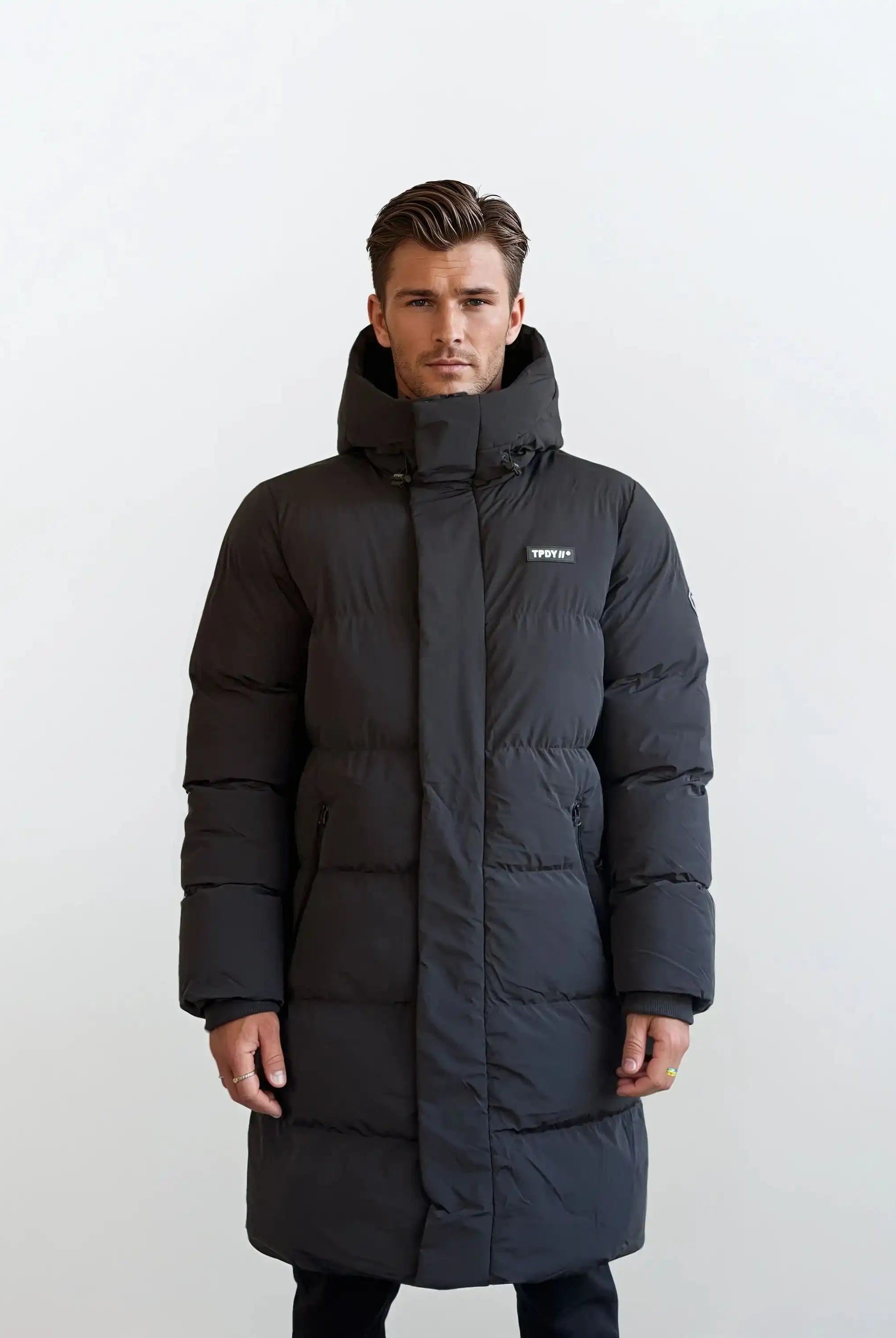 Vor weißem Hintergrund trägt ein Mann den Herren Parka mit fester Kapuze im Regular Fit von trueprodigy. Der wasserabweisende Parka hat sichtbare Nähte, ein kleines weißes Logo auf der linken Brust und die Hände des Mannes ruhen an seinen Seiten.