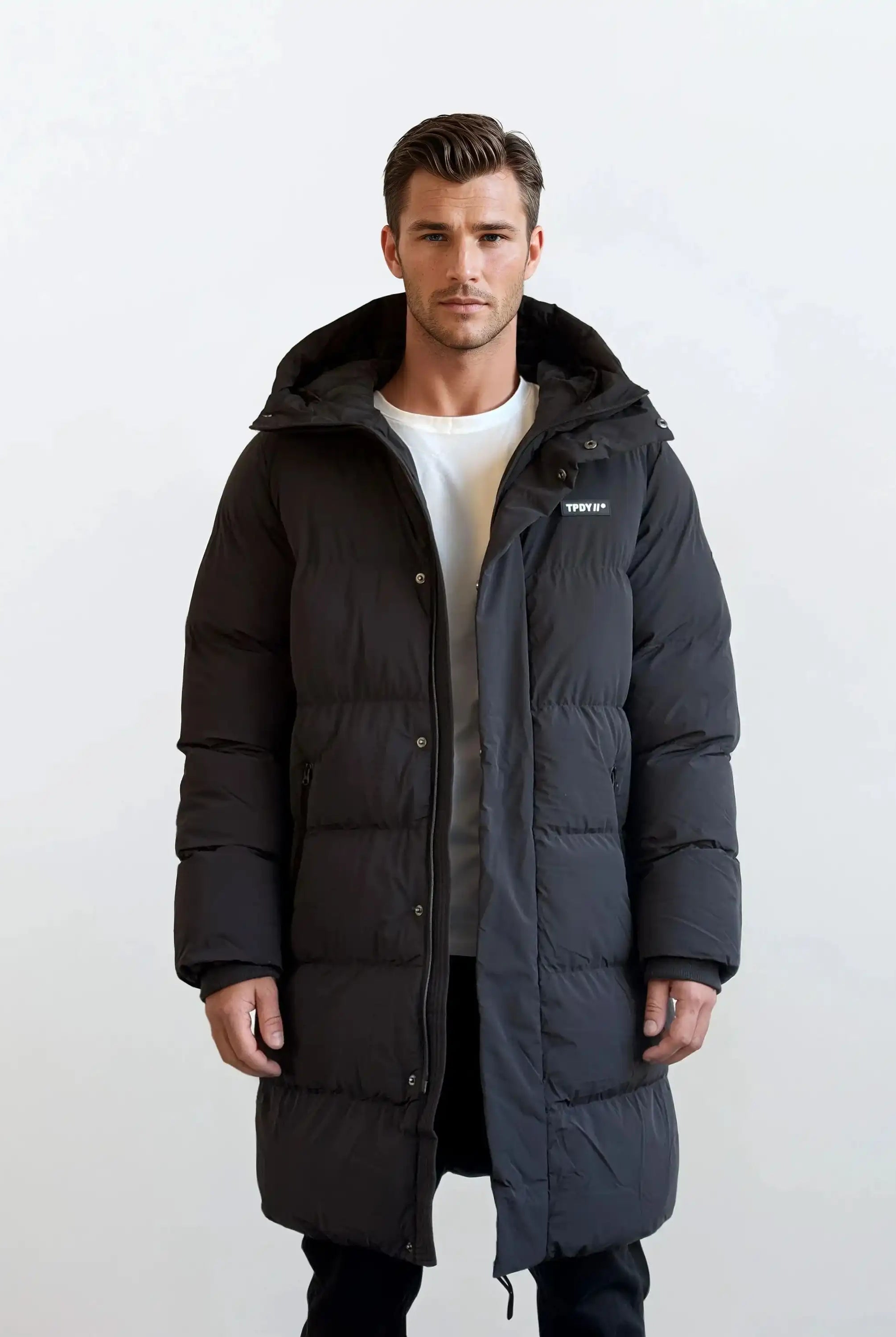 Ein Mann trägt den Herren Parka mit fester Kapuze im Regular Fit von trueprodigy über einem weißen T-Shirt und schwarzen Hosen vor weißem Hintergrund. Die gesteppte Jacke hat ein kleines Logo auf der Brust.