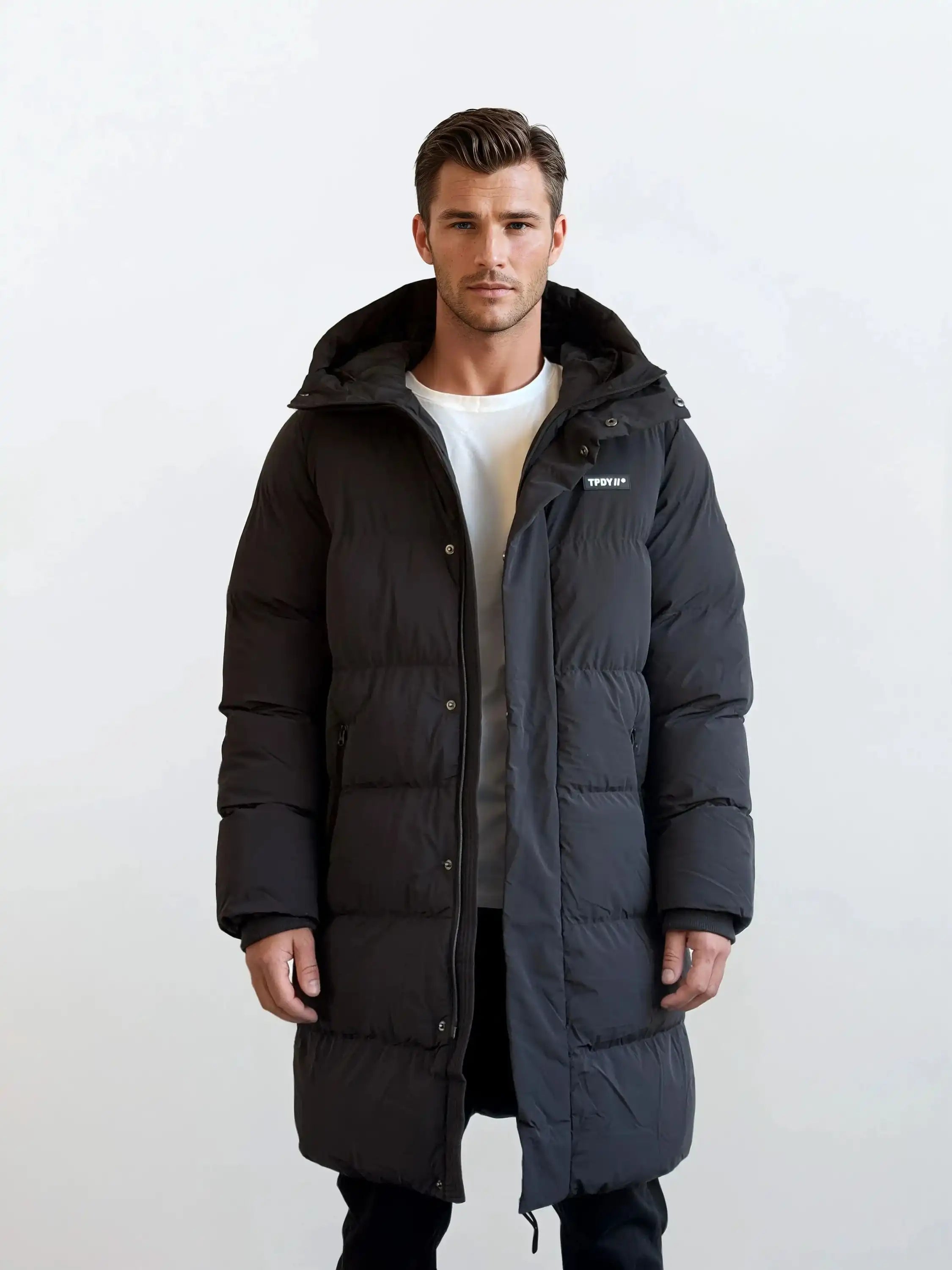 Ein Mann trägt den Herren Parka mit fester Kapuze im Regular Fit von trueprodigy über einem weißen T-Shirt und schwarzen Hosen vor weißem Hintergrund. Die gesteppte Jacke hat ein kleines Logo auf der Brust.