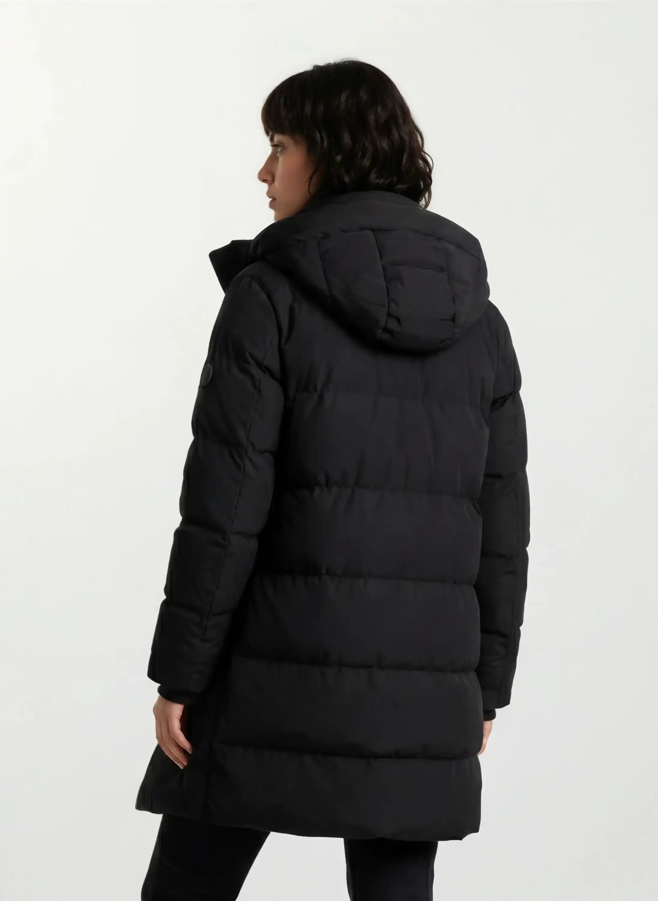 Abgebildet ist eine Person mit kurzen dunklen Haaren von hinten, die den trueprodigy Damen Parka mit fester Kapuze im Regular Fit in Schwarz trägt, der vor einem schlichten weißen Hintergrund wasserabweisend wirkt.