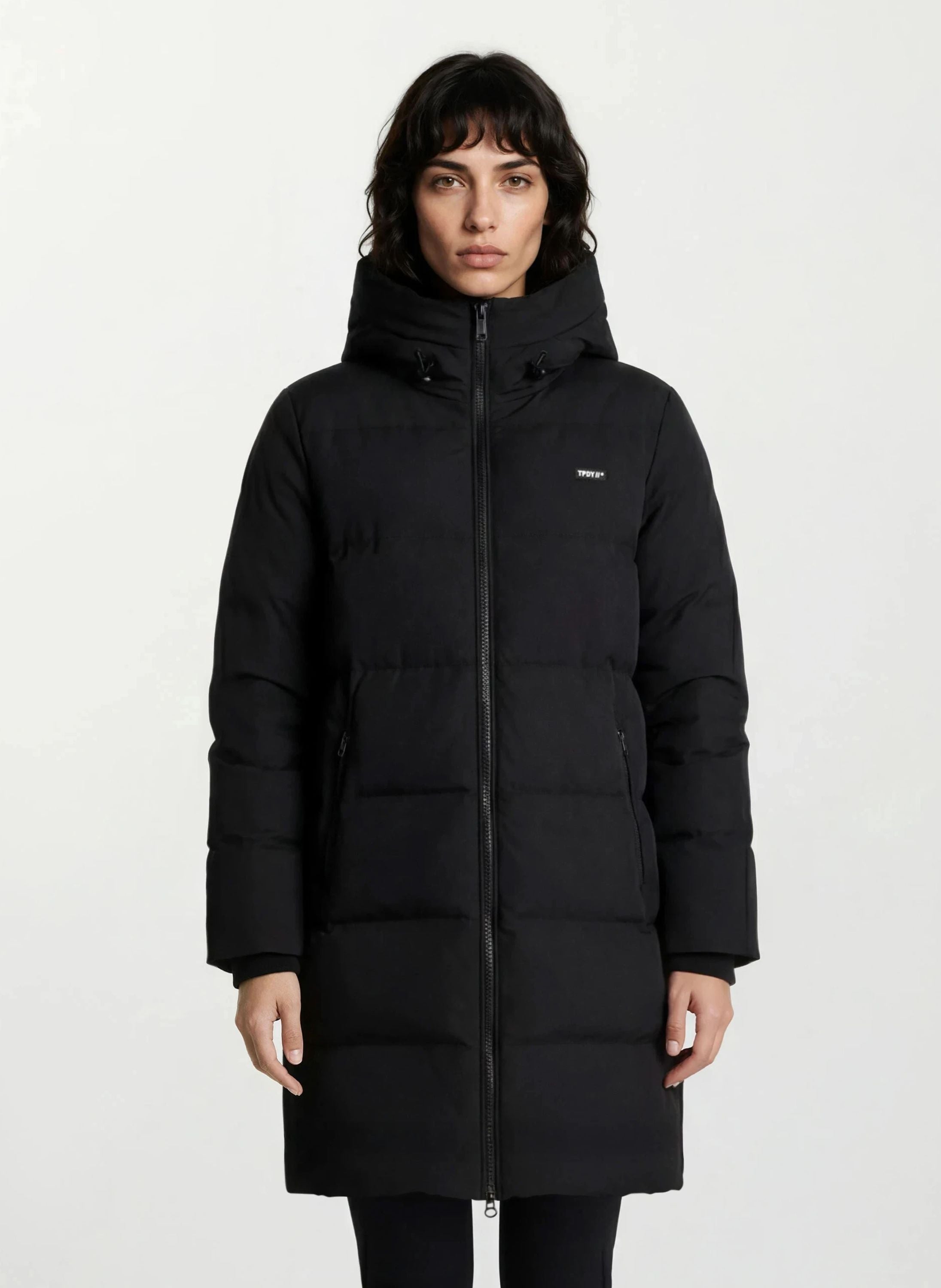 Eine Person mit kurzen dunklen Haaren trägt einen Damen Parka mit fester Kapuze im Regular Fit von trueprodigy und steht vor einem schlichten weißen Hintergrund.