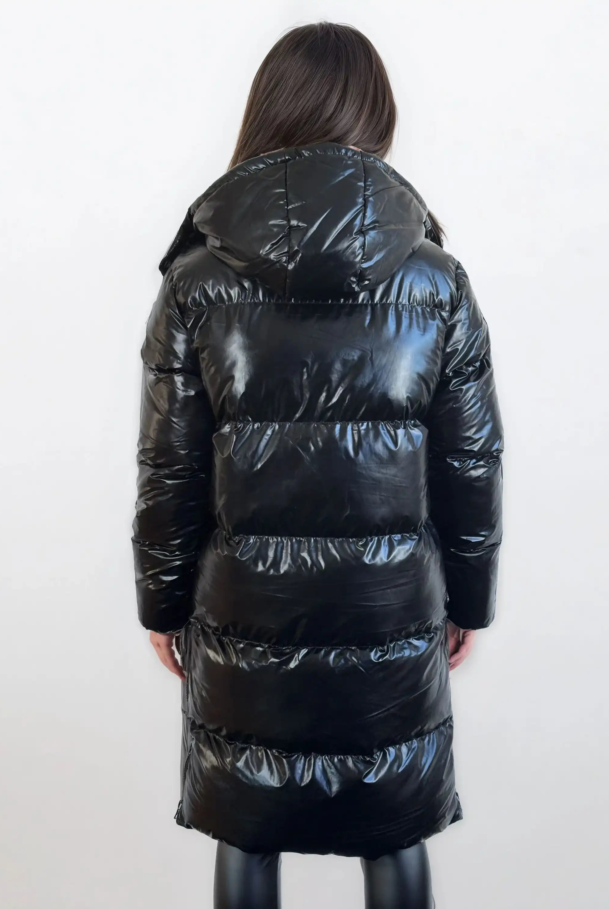 Man sieht eine Person mit langen braunen Haaren von hinten, die eine trueprodigy Damen Winterjacke mit hochglänzender Oberfläche im Regular Fit und eine schwarze Hose trägt und vor einem schlichten weißen Hintergrund steht.