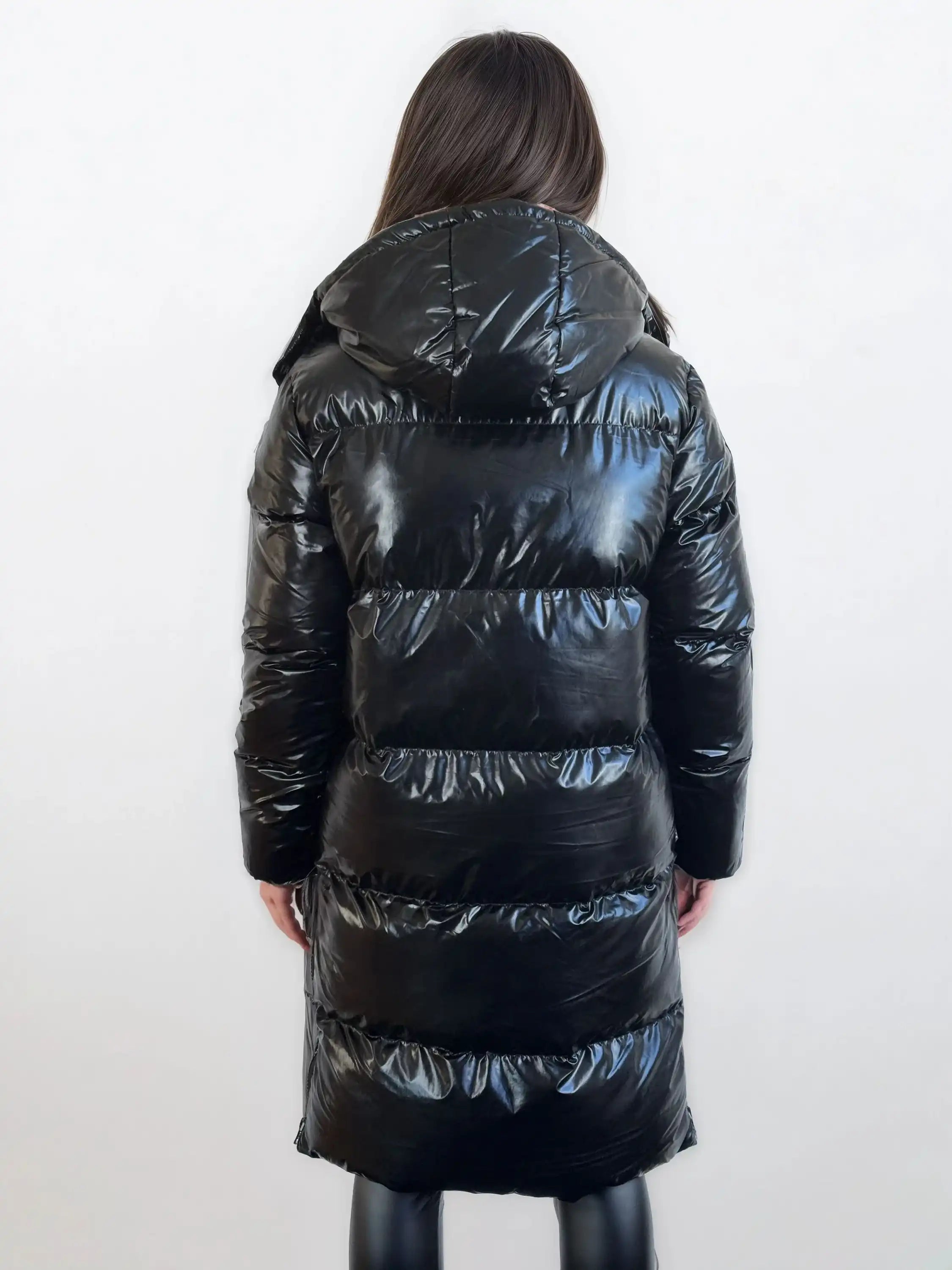 Man sieht eine Person mit langen braunen Haaren von hinten, die eine trueprodigy Damen Winterjacke mit hochglänzender Oberfläche im Regular Fit und eine schwarze Hose trägt und vor einem schlichten weißen Hintergrund steht.