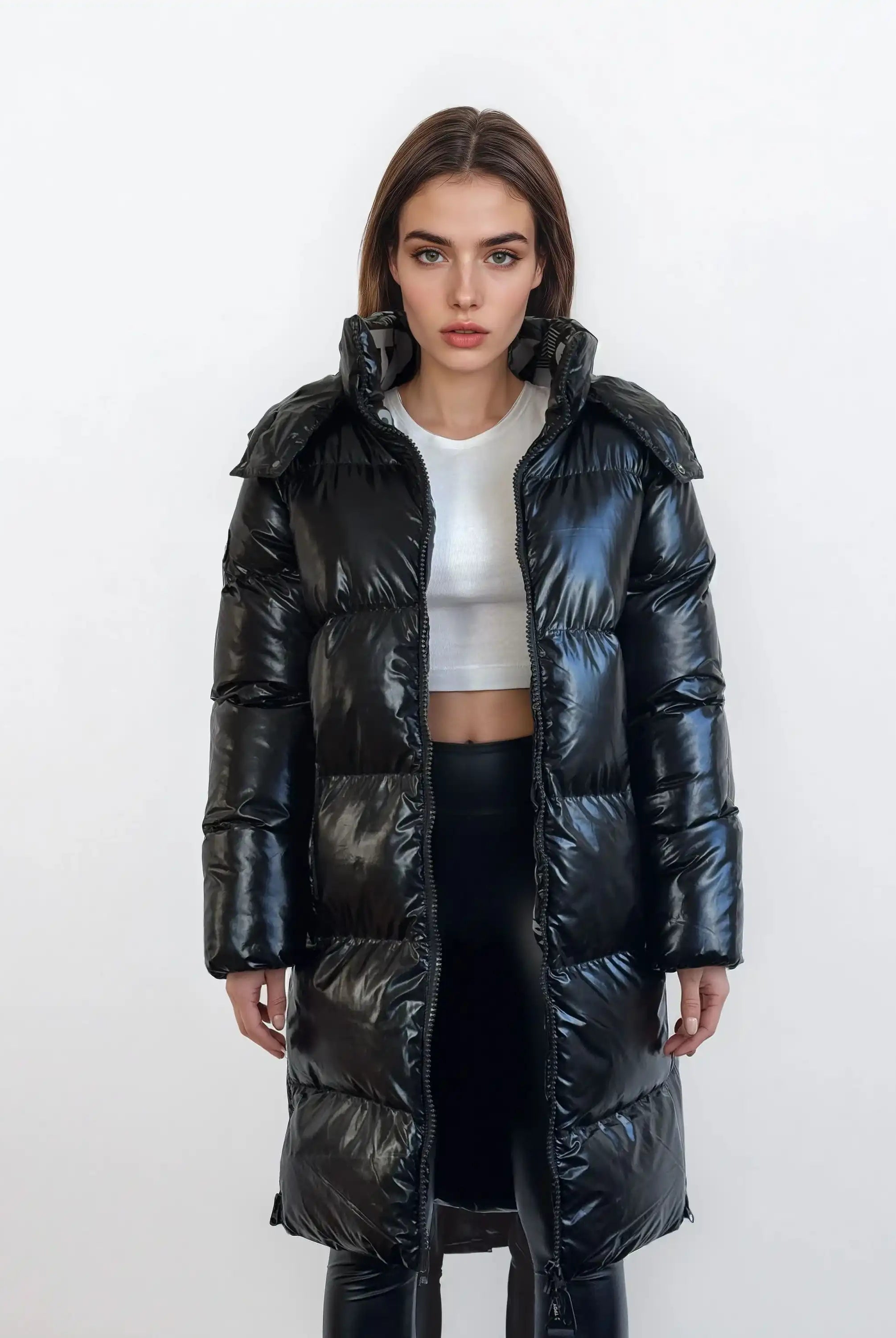 Eine Person steht vor einem weißen Hintergrund, trägt eine trueprodigy Damen Winterjacke mit hochglänzender Oberfläche im Regular Fit über einem weißen Crop Top und einer schwarzen Hose und schaut mit neutralem Blick in die Kamera.