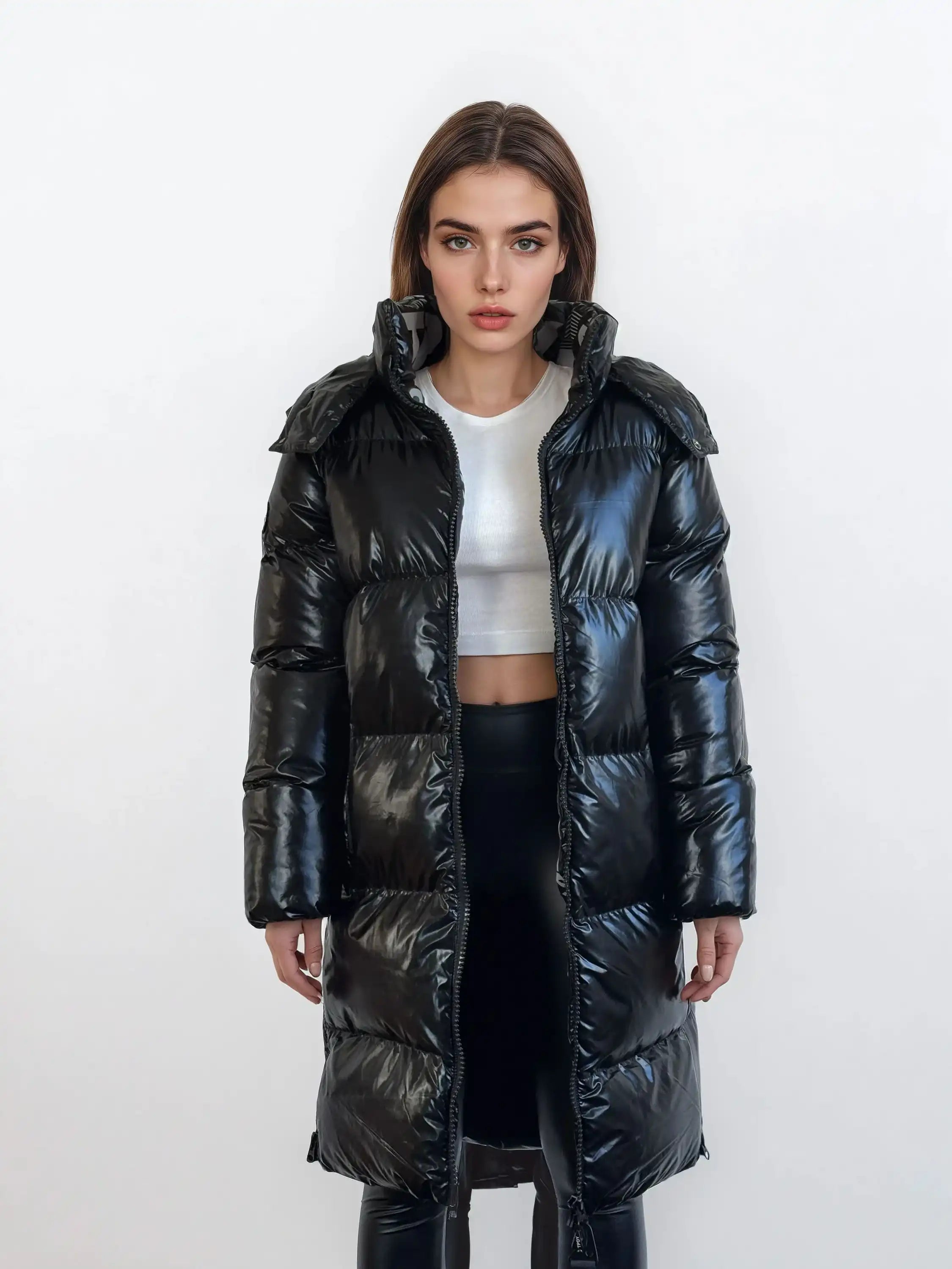 Eine Person steht vor einem weißen Hintergrund, trägt eine trueprodigy Damen Winterjacke mit hochglänzender Oberfläche im Regular Fit über einem weißen Crop Top und einer schwarzen Hose und schaut mit neutralem Blick in die Kamera.