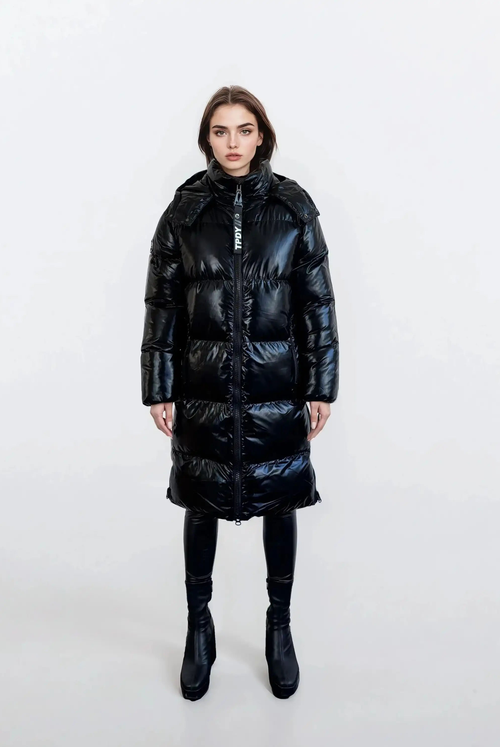 Eine Person steht mit dem Gesicht nach vorne vor einem schlichten weißen Hintergrund und trägt die trueprodigy Damen Winterjacke mit hochglänzender Oberfläche im Regular Fit, gepaart mit einer schwarzen Hose und schwarzen Ankle Boots.
