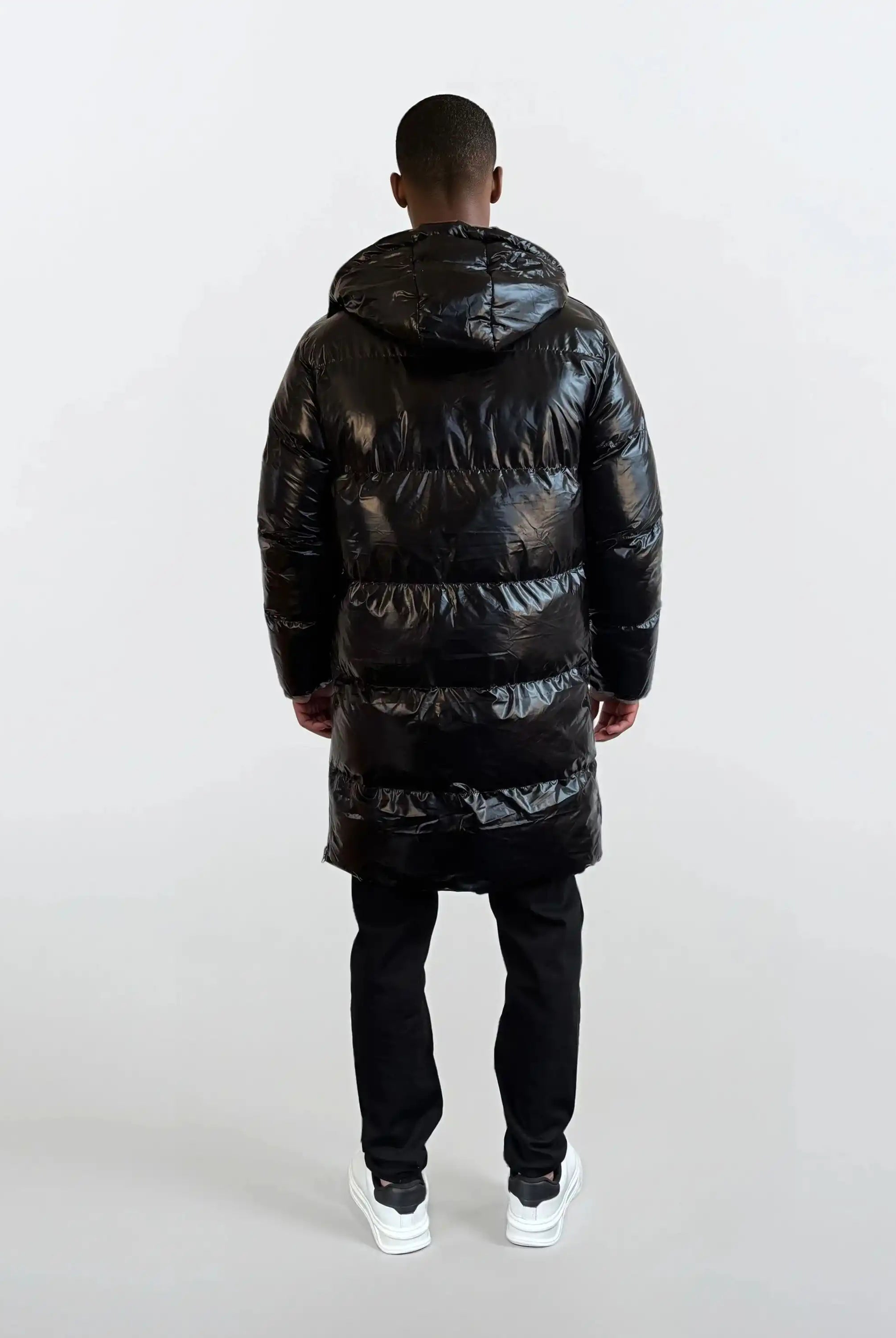 Eine Person steht von der Kamera abgewandt und trägt eine trueprodigy Herren Winterjacke mit hochglänzender Oberfläche im Regular Fit, eine schwarze Hose und weiße Turnschuhe. Der Hintergrund ist einfarbig und hell.