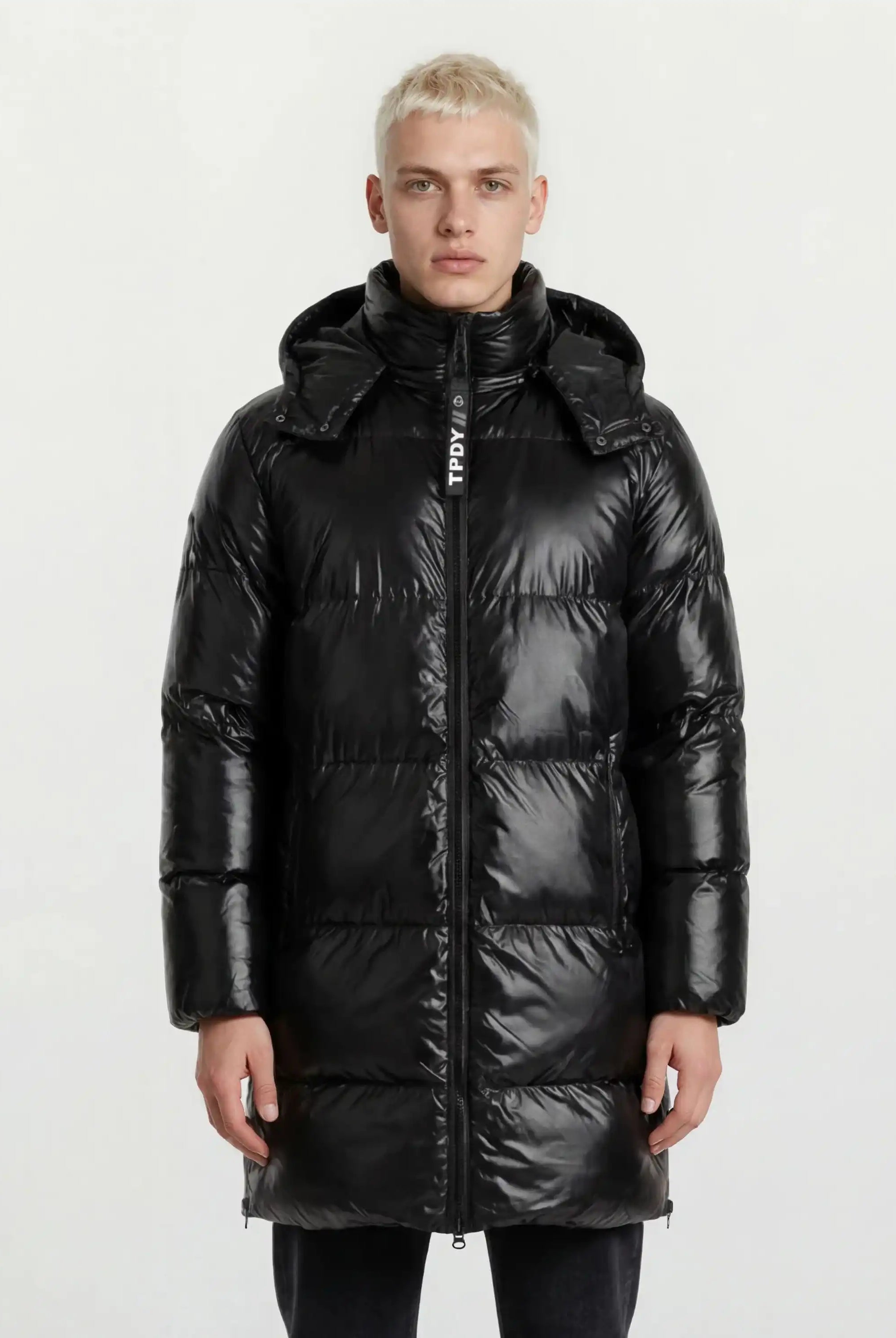 Eine Person blickt vor einem hellen Hintergrund nach vorne und trägt die trueprodigy Herren Winterjacke mit hochglänzender Oberfläche im Regular Fit, die mit einem hohen Kragen, einer abnehmbaren Kapuze und einem Frontreißverschluss für einen eleganten Look ausgestattet ist.