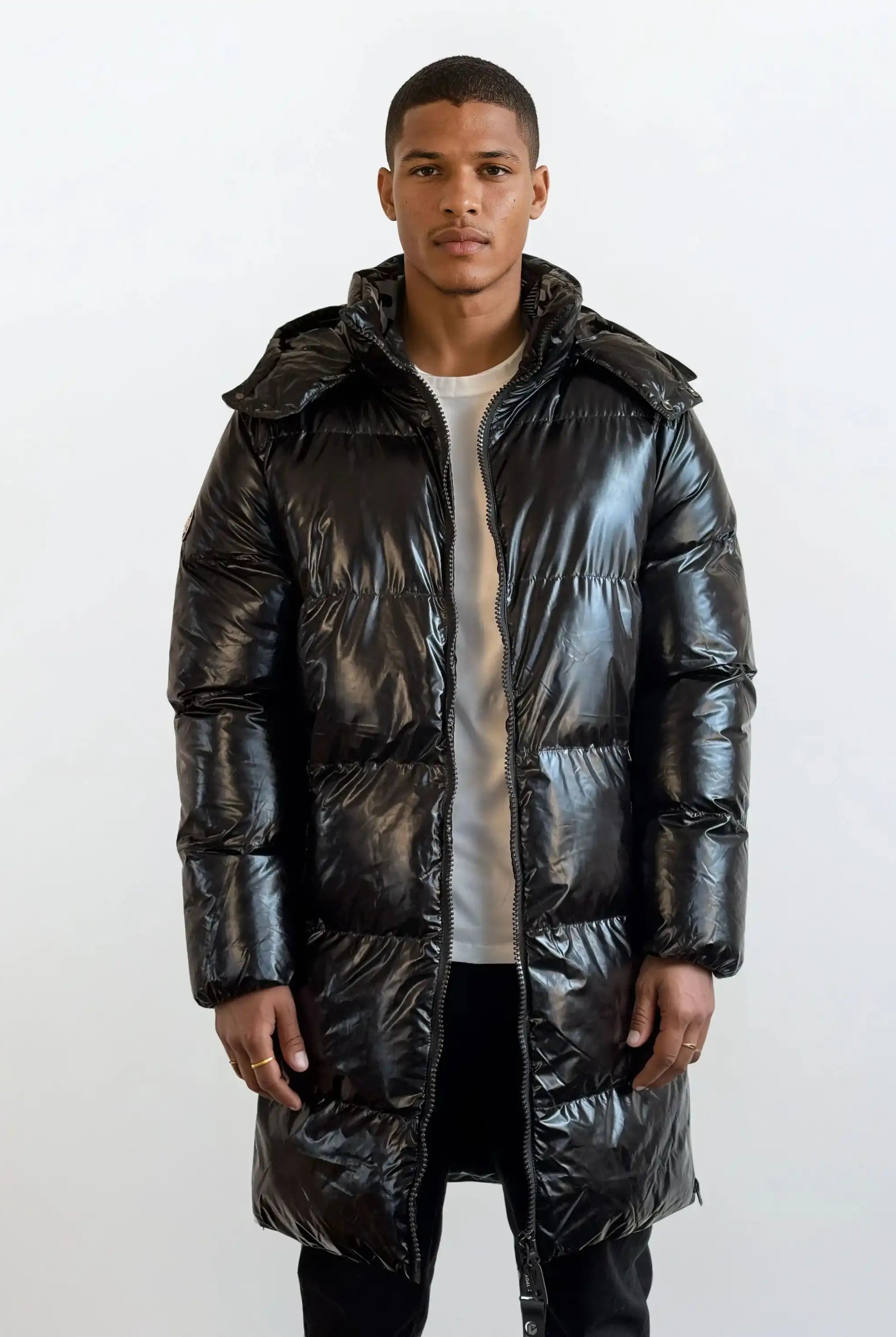 Eine Person steht mit dem Gesicht nach vorne und trägt eine trueprodigy Herren Winterjacke mit hochglänzender Oberfläche im Regular Fit über einem hellen Hemd und einer dunklen Hose vor einem schlichten weißen Hintergrund.