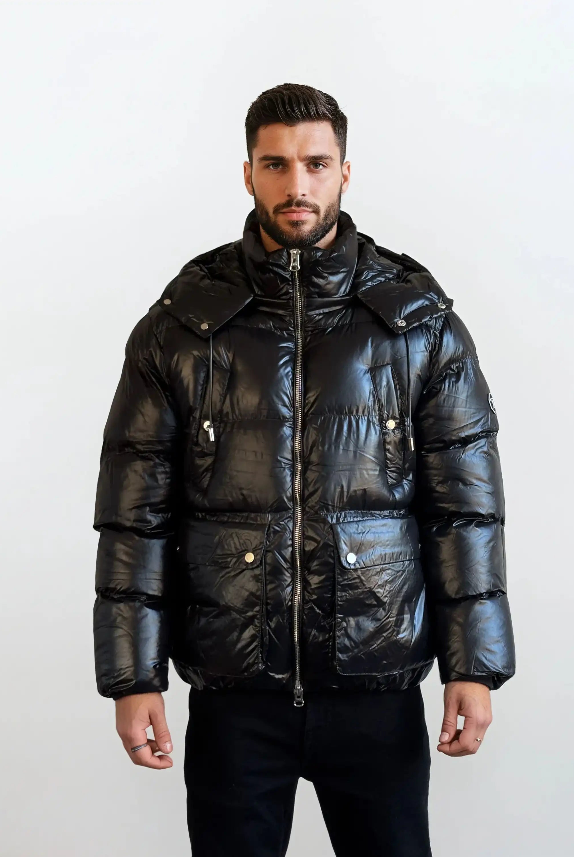 Ein Mann mit kurzem, dunklem Haar und Bart trägt die trueprodigy Herren Winterjacke mit hochglänzender Oberfläche im Regular Fit, ausgestattet mit großen Fronttaschen, stehend vor einem schlichten, hellen Hintergrund.