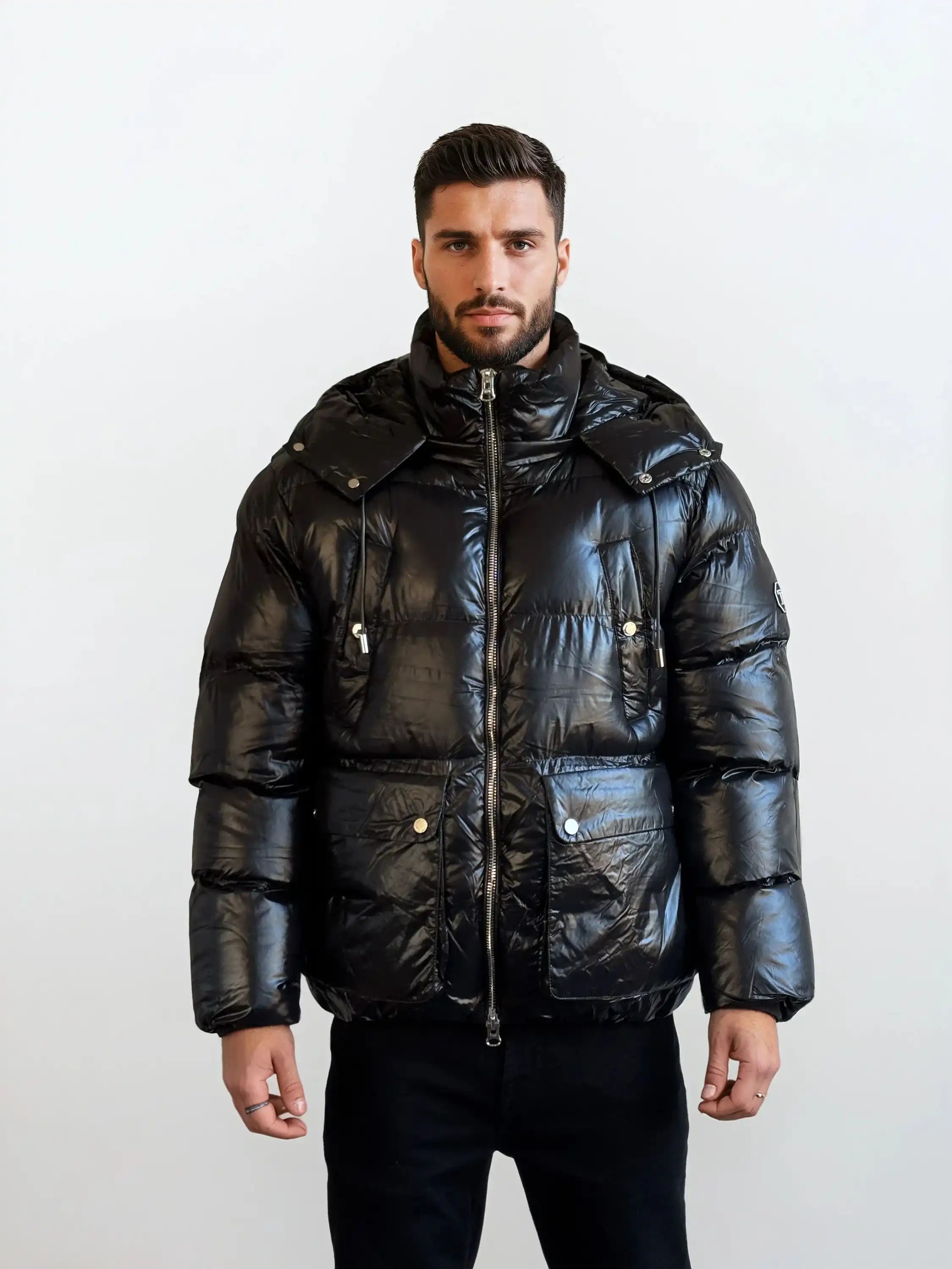 Ein Mann mit kurzem, dunklem Haar und Bart trägt die trueprodigy Herren Winterjacke mit hochglänzender Oberfläche im Regular Fit, ausgestattet mit großen Fronttaschen, stehend vor einem schlichten, hellen Hintergrund.