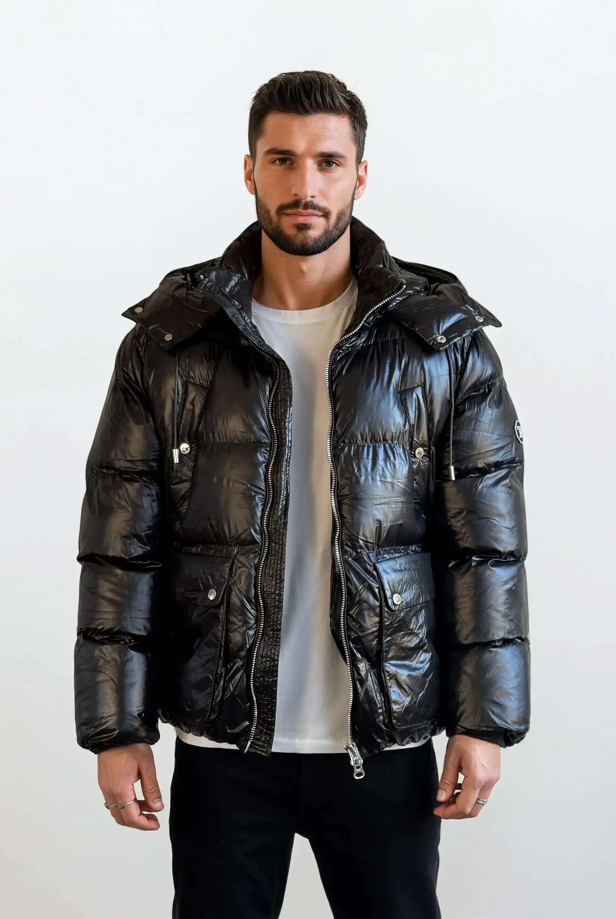 Ein Mann mit kurzen dunklen Haaren und einem Bart steht mit dem Gesicht nach vorne und trägt die trueprodigy Herren Winterjacke mit hochglänzender Oberfläche im Regular Fit über einem weißen T-Shirt und einer schwarzen Hose vor einem schlichten hellen Hintergrund.