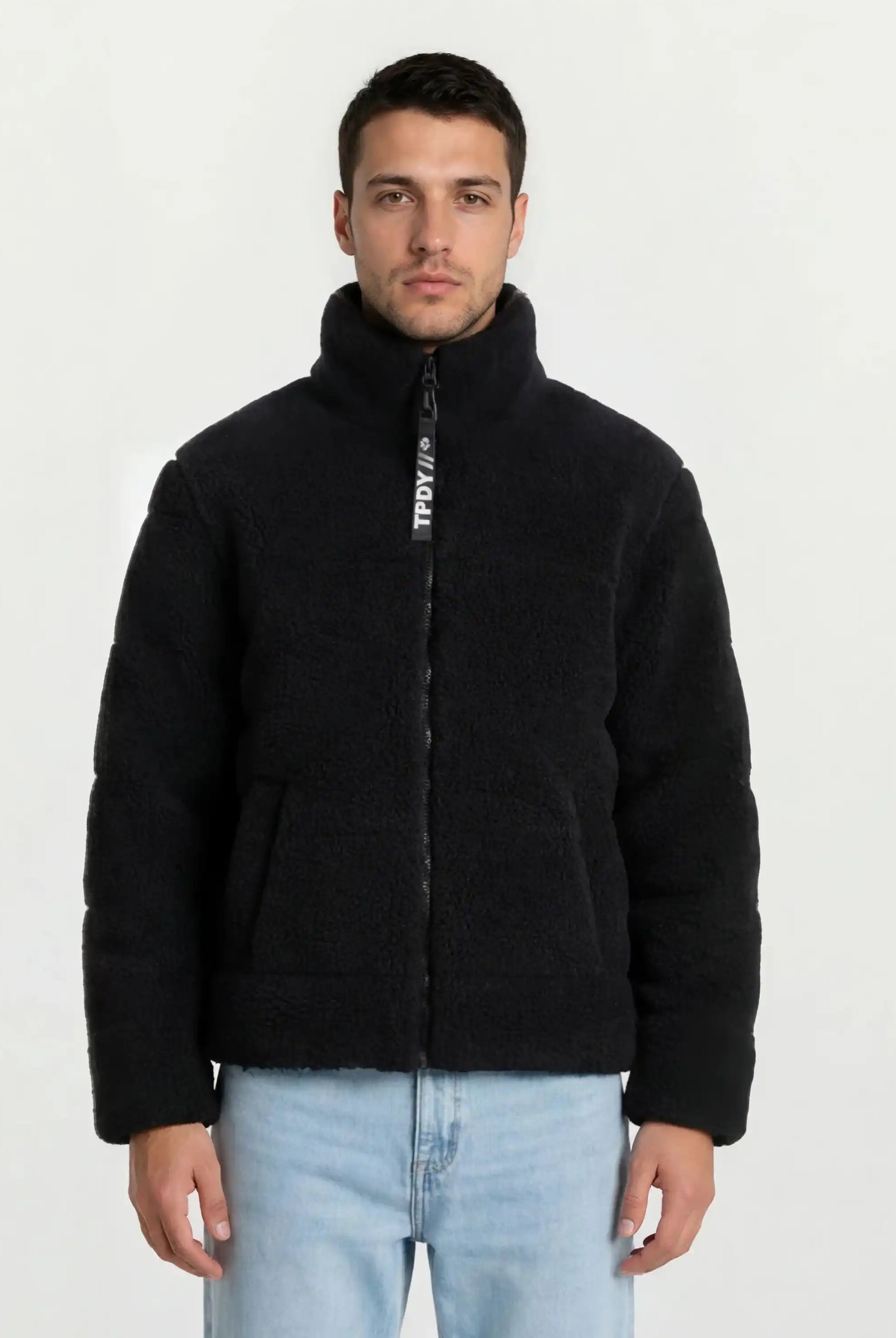 Ein Mann steht mit dem Gesicht nach vorne und trägt eine trueprodigy Herren Winterjacke mit flauschiger Sherpa-Oberfläche im Oversized Fit und hellblaue Jeans. Der Hintergrund ist einfarbig weiß.