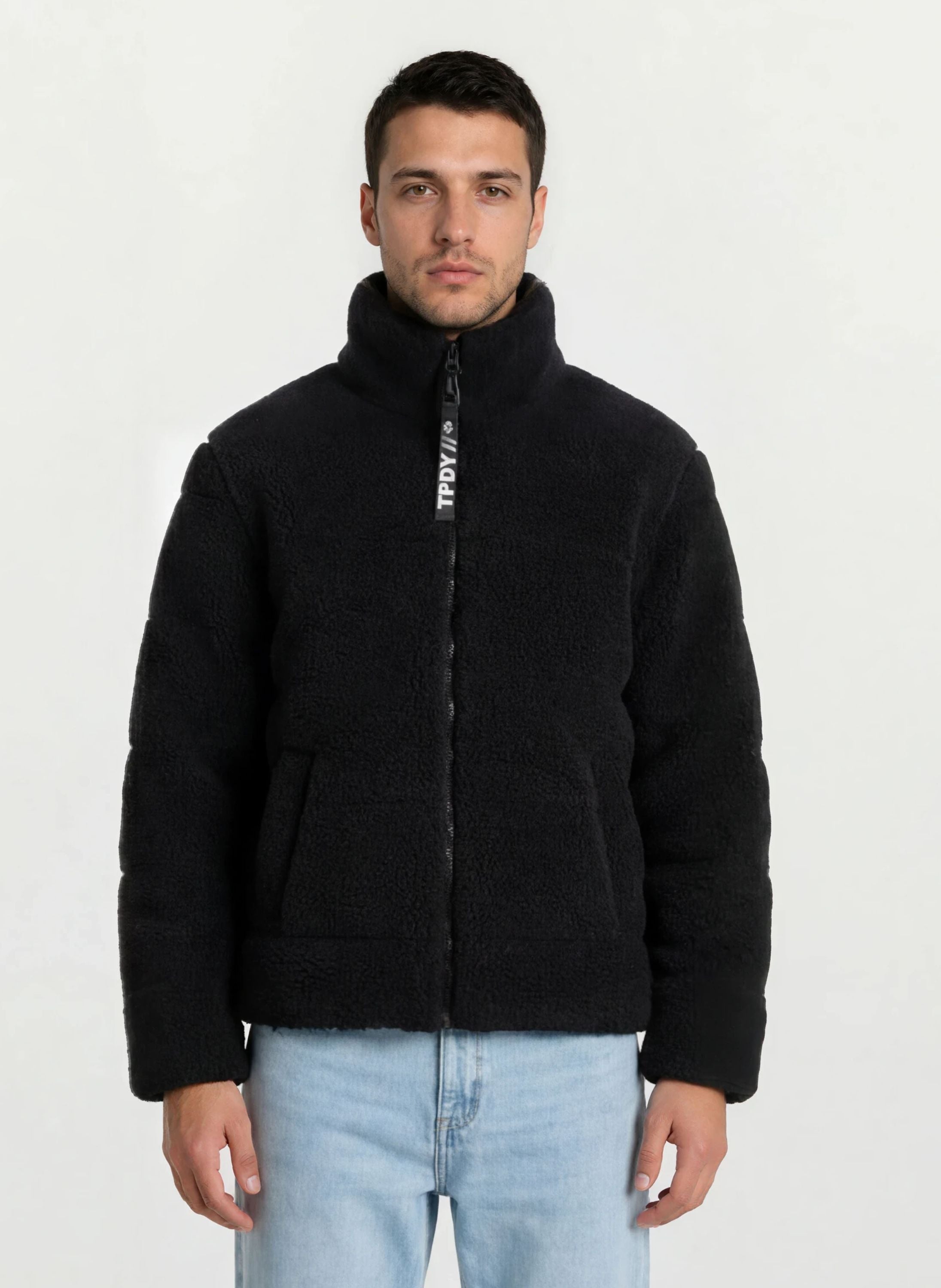 Ein Mann steht mit dem Gesicht nach vorne und trägt eine trueprodigy Herren Winterjacke mit flauschiger Sherpa-Oberfläche im Oversized Fit und hellblaue Jeans. Der Hintergrund ist einfarbig weiß.