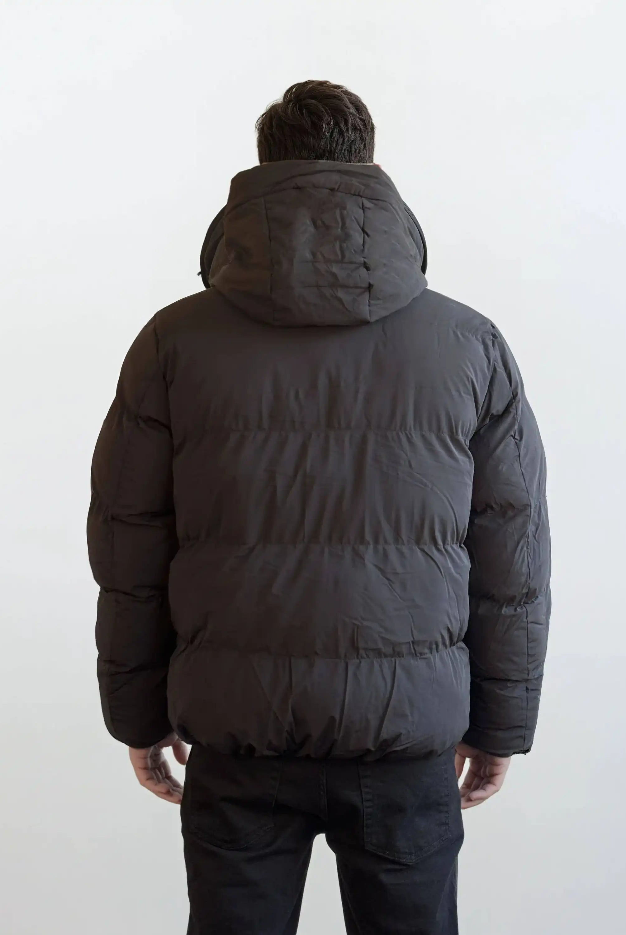 Eine Person, die eine trueprodigy Herren Winterjacke mit fester Kapuze im Oversized Fit trägt, schaut von der Kamera weg vor einem schlichten, hellen Hintergrund.