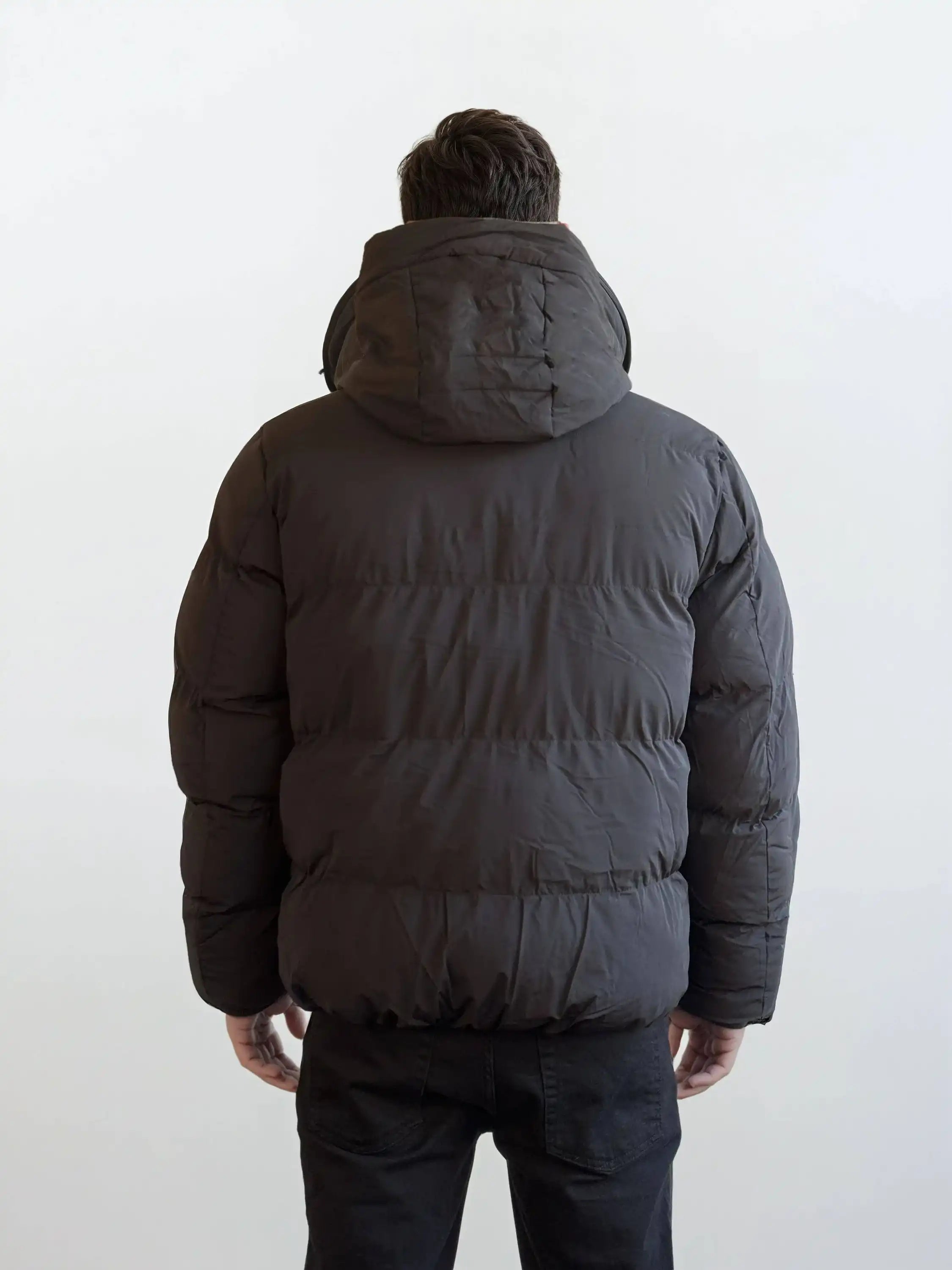 Eine Person, die eine trueprodigy Herren Winterjacke mit fester Kapuze im Oversized Fit trägt, schaut von der Kamera weg vor einem schlichten, hellen Hintergrund.