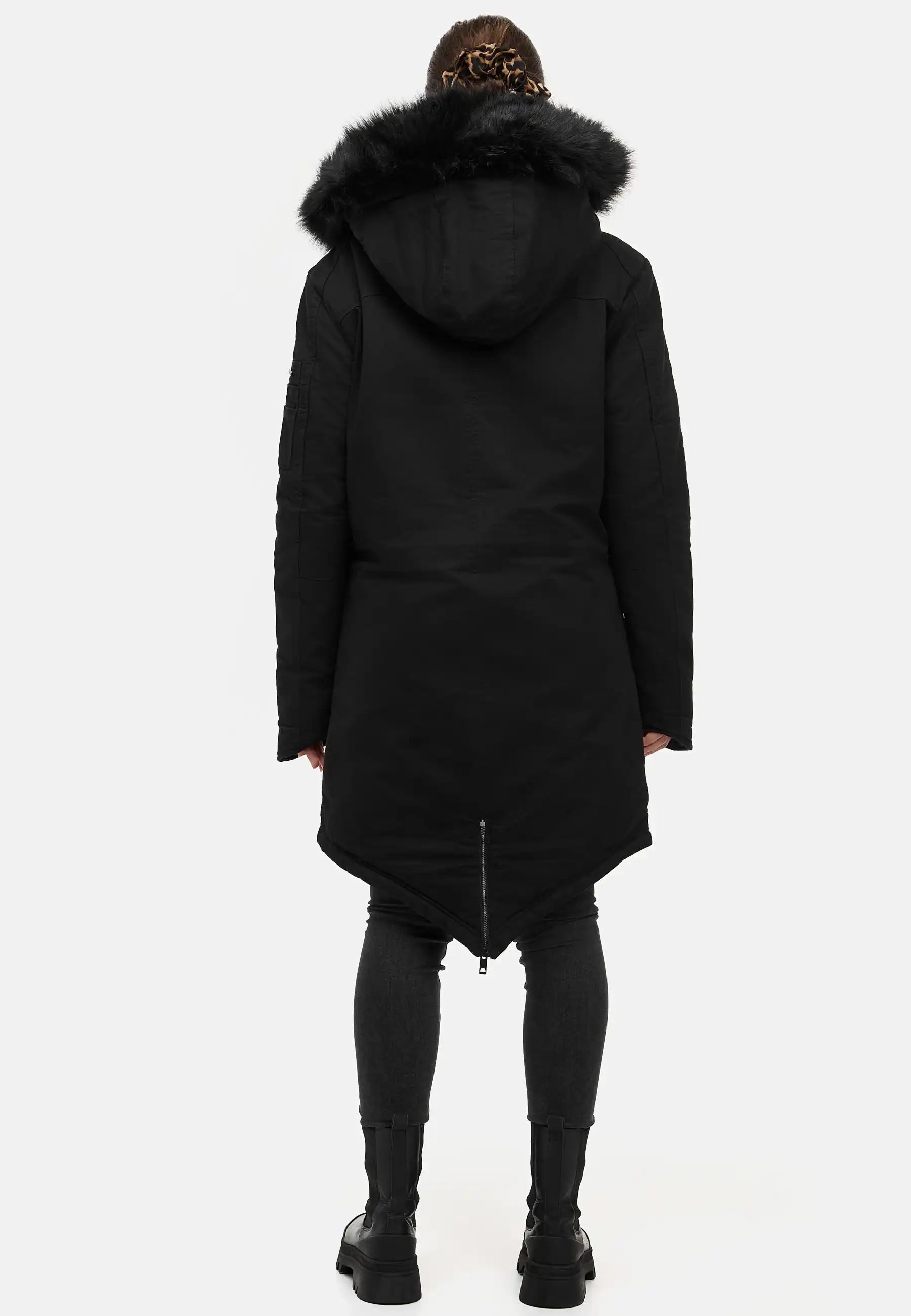 Eine Person blickt von der Kamera weg und trägt den trueprodigy Harvey F Damenparka mit Kapuze und Kunstfell, eine taillierte dunkle Hose und schwarze Stiefel. Der Hintergrund ist einfarbig weiß.