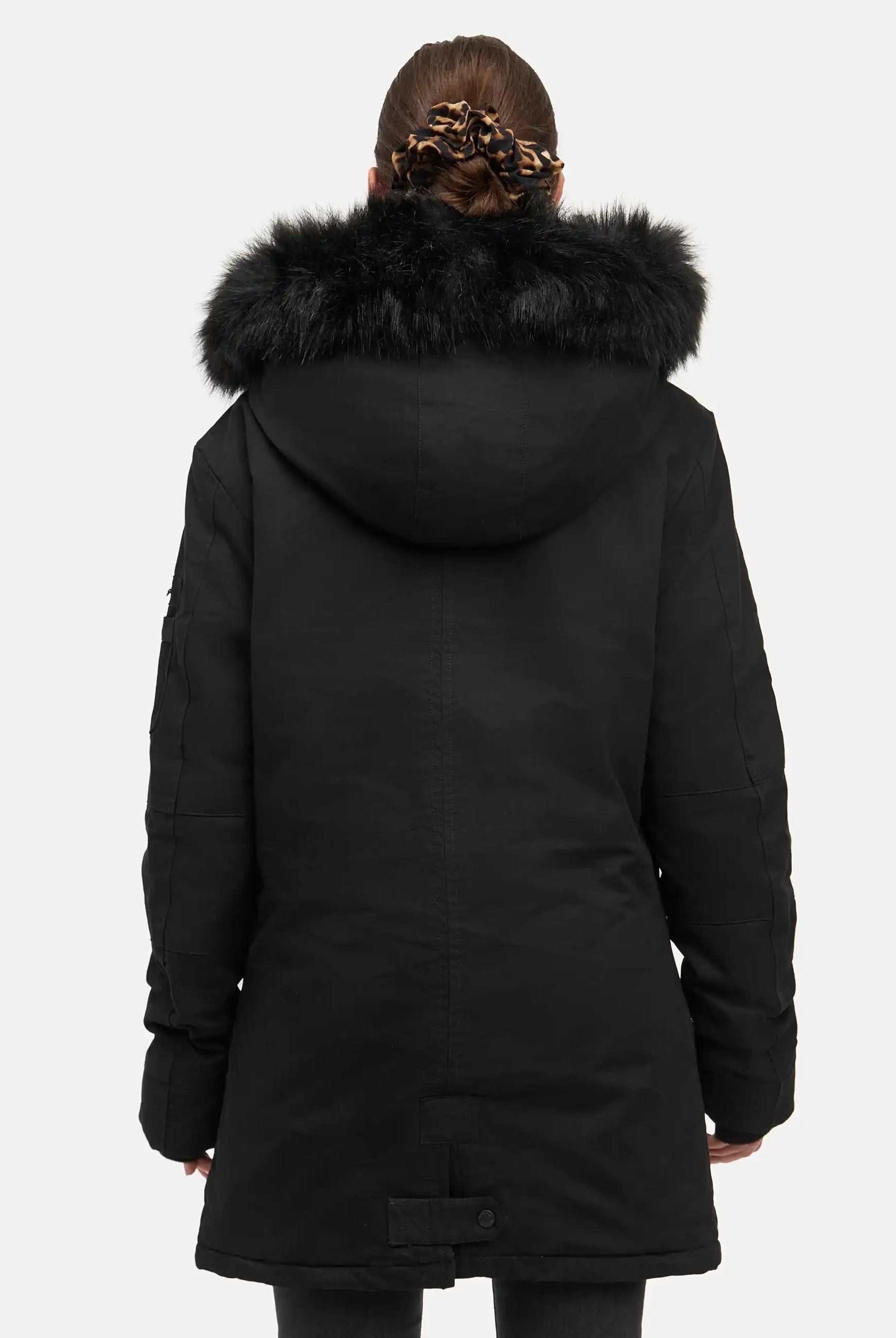 Eine Person mit braunen Haaren in einer Haarspange mit Leopardenmuster ist von hinten zu sehen, die den trueprodigy Julius F Parka mit Kapuze und Kunstfell in Schwarz trägt. Der Parka hat eine große Kapuze mit schwarzem Kunstfellbesatz. Der Hintergrund ist einfarbig und hell.