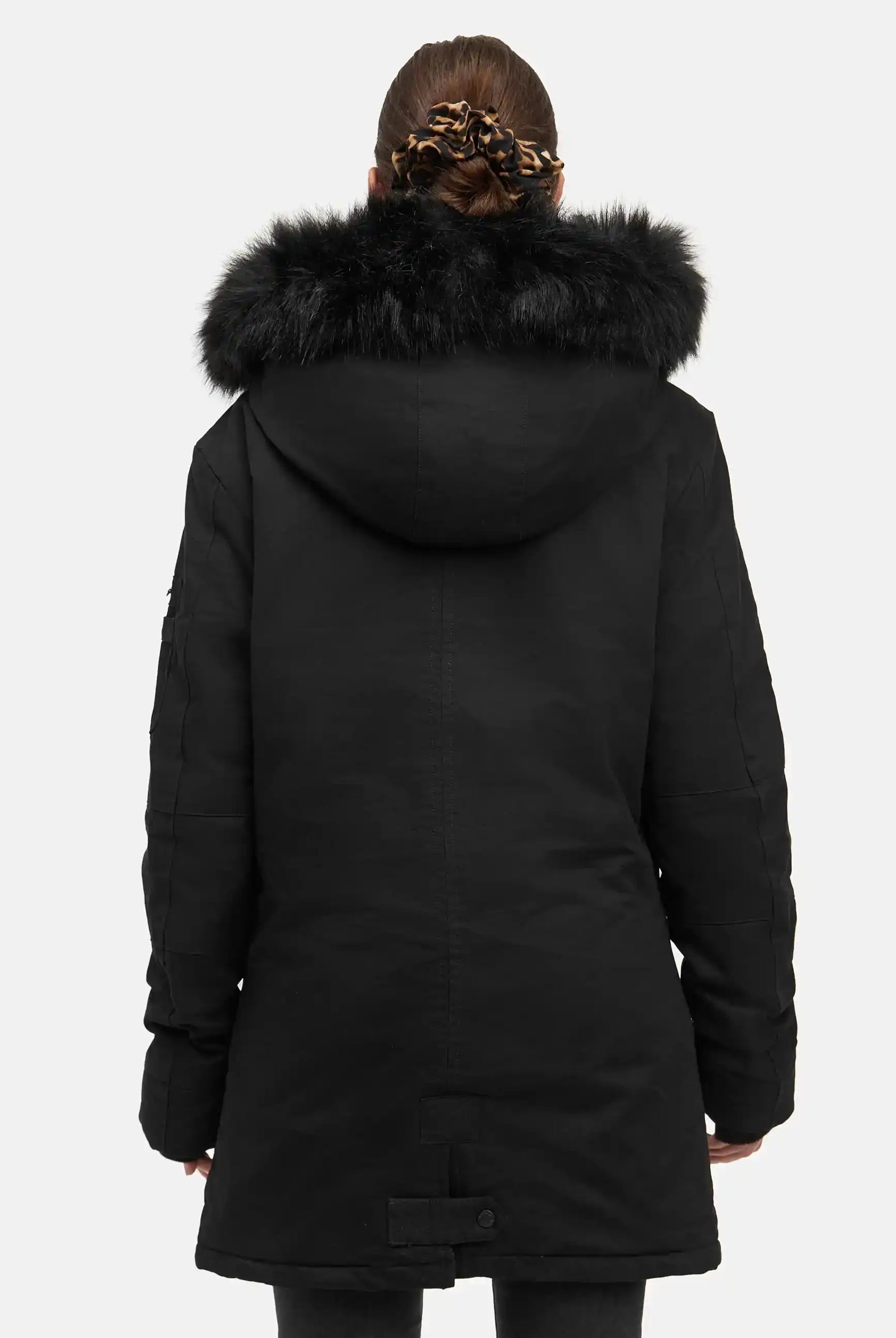 Eine Person mit braunen Haaren in einer Haarspange mit Leopardenmuster ist von hinten zu sehen, die den trueprodigy Julius F Parka mit Kapuze und Kunstfell in Schwarz trägt. Der Parka hat eine große Kapuze mit schwarzem Kunstfellbesatz. Der Hintergrund ist einfarbig und hell.