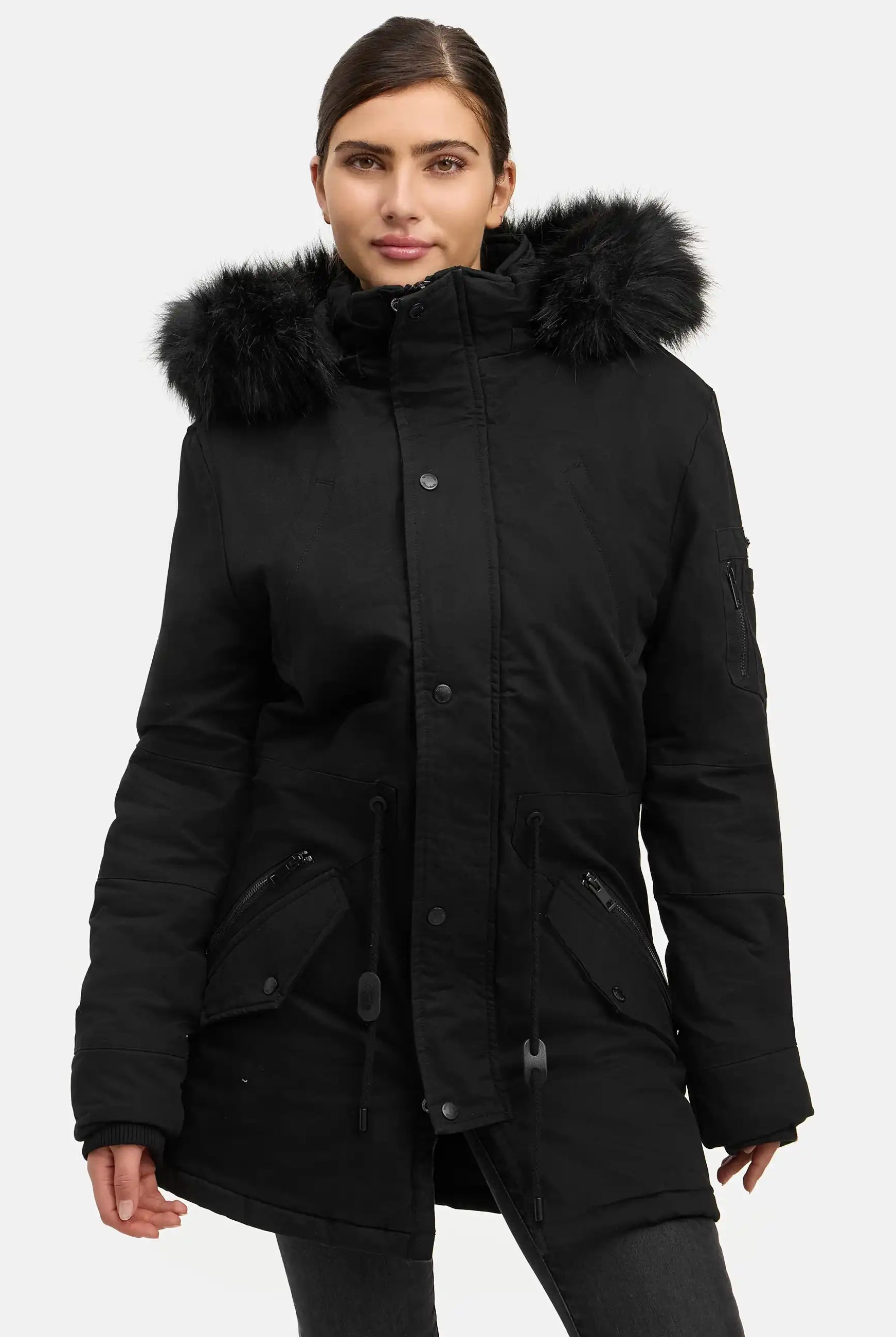 Eine Person steht vor einem weißen Hintergrund und trägt den trueprodigy Julius F Parka mit Kapuze und Kunstfell, einen schwarzen Damenparka mit Kunstfellbesatz, Frontreißverschluss, Knöpfen und mehreren Taschen.