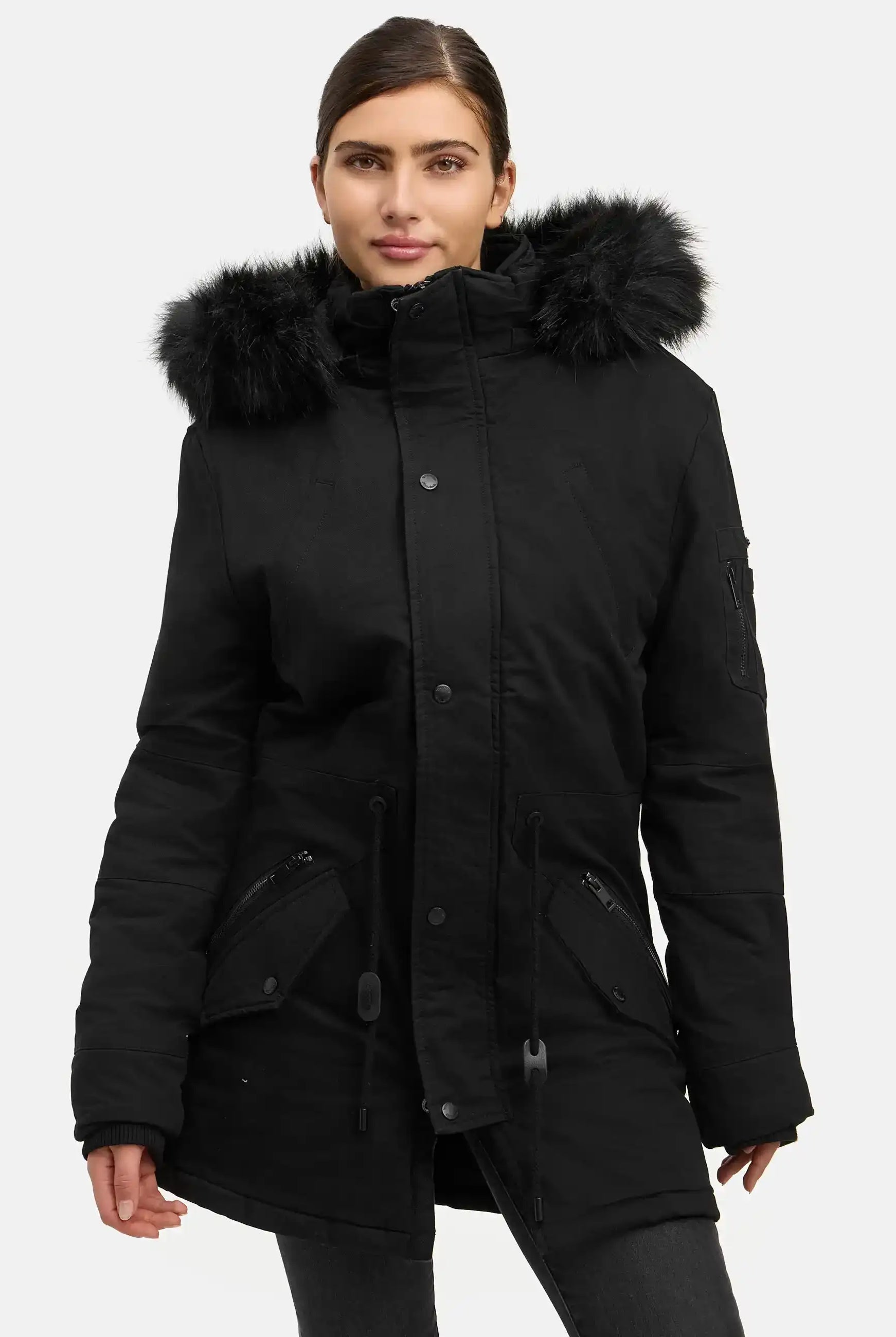 Eine Person steht vor einem weißen Hintergrund und trägt den trueprodigy Julius F Parka mit Kapuze und Kunstfell, einen schwarzen Damenparka mit Kunstfellbesatz, Frontreißverschluss, Knöpfen und mehreren Taschen.