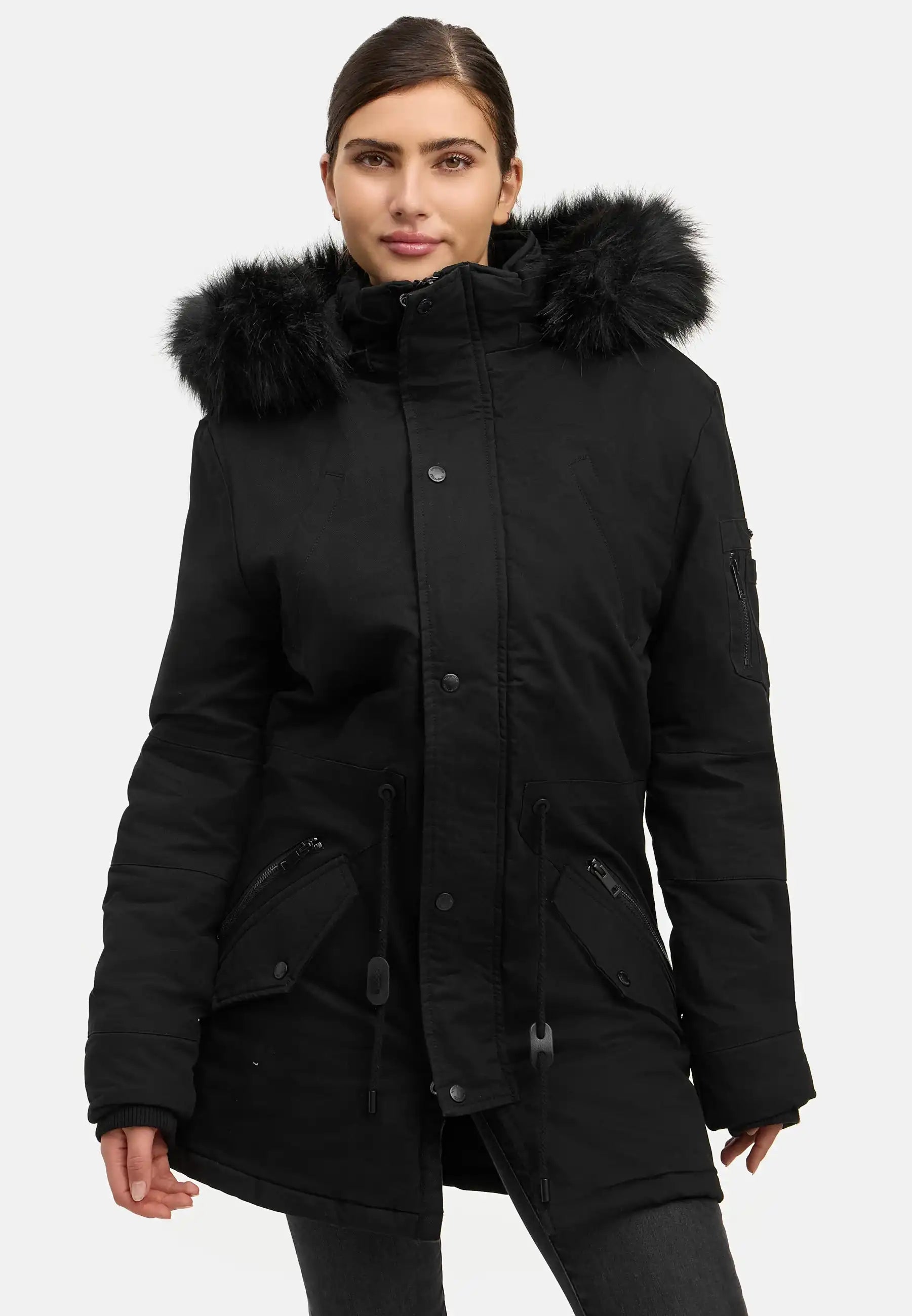 Eine Person steht vor einem weißen Hintergrund und trägt den trueprodigy Julius F Parka mit Kapuze und Kunstfell, einen schwarzen Damenparka mit Kunstfellbesatz, Frontreißverschluss, Knöpfen und mehreren Taschen.