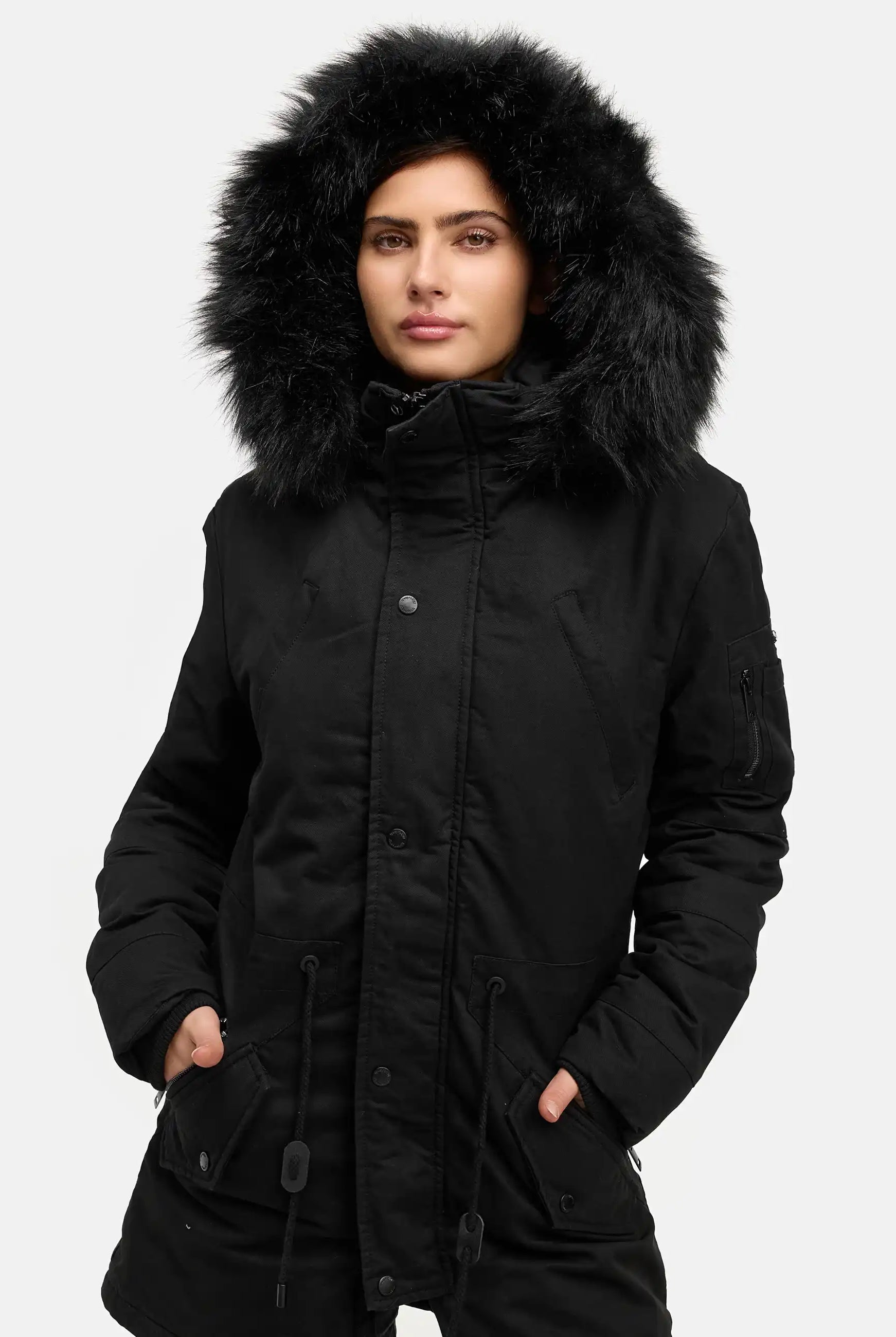 Eine Person modelliert den trueprodigy Julius F Parka mit Kapuze und Kunstfell in Schwarz, mit pelzgefütterter Kapuze und legerer Passform, stehend mit den Händen in den Taschen vor einem schlichten weißen Hintergrund.