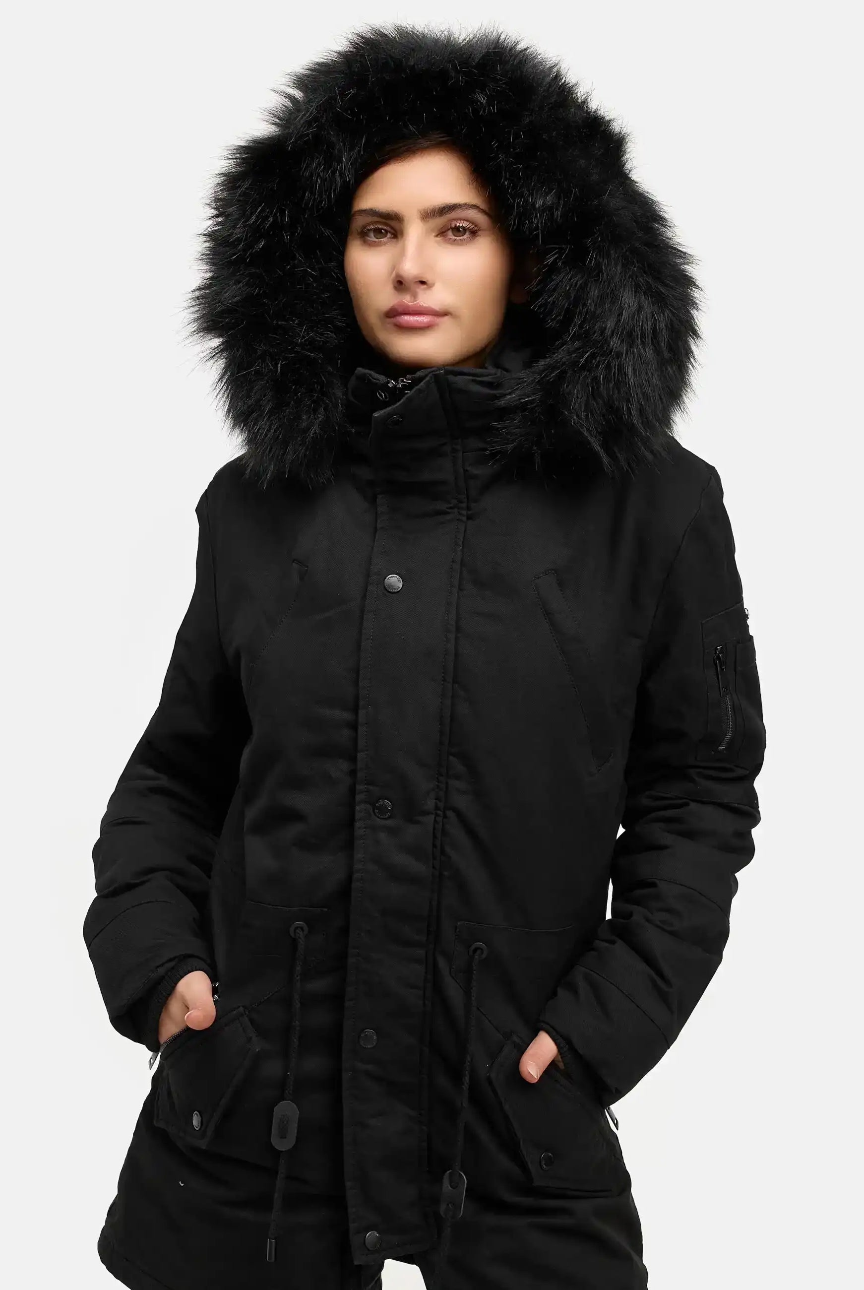 Eine Person modelliert den trueprodigy Julius F Parka mit Kapuze und Kunstfell in Schwarz, mit pelzgefütterter Kapuze und legerer Passform, stehend mit den Händen in den Taschen vor einem schlichten weißen Hintergrund.